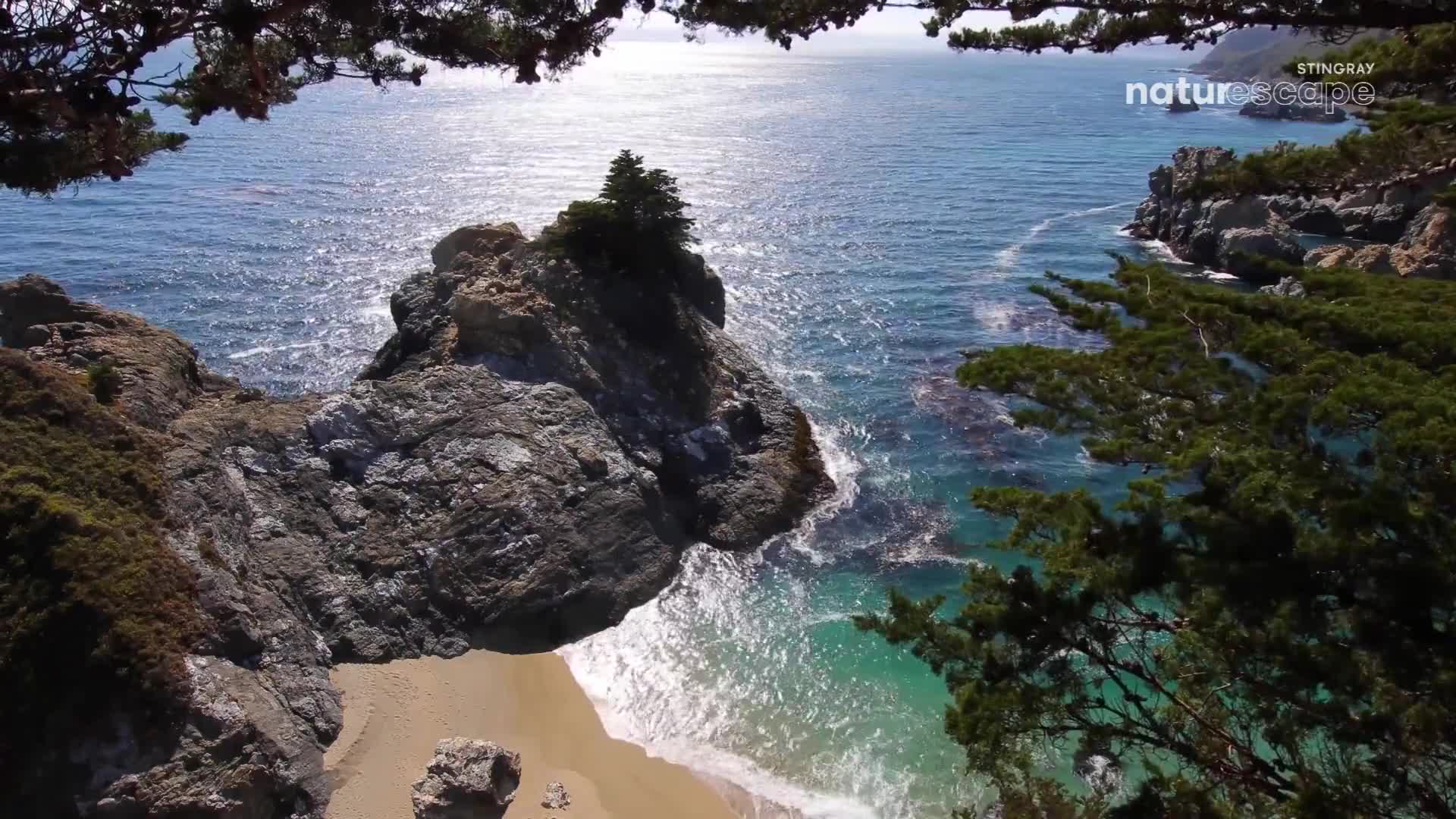 The ocean crashes against the rocky shore, sending white foam onto the sand. Sunlight glints off the water's surface, illuminating the clear turquoise shallows. The ocean crashes against the rocky shore, sending white foam onto the sand. Sunlight glints off the water's surface, illuminating the clear turquoise shallows.