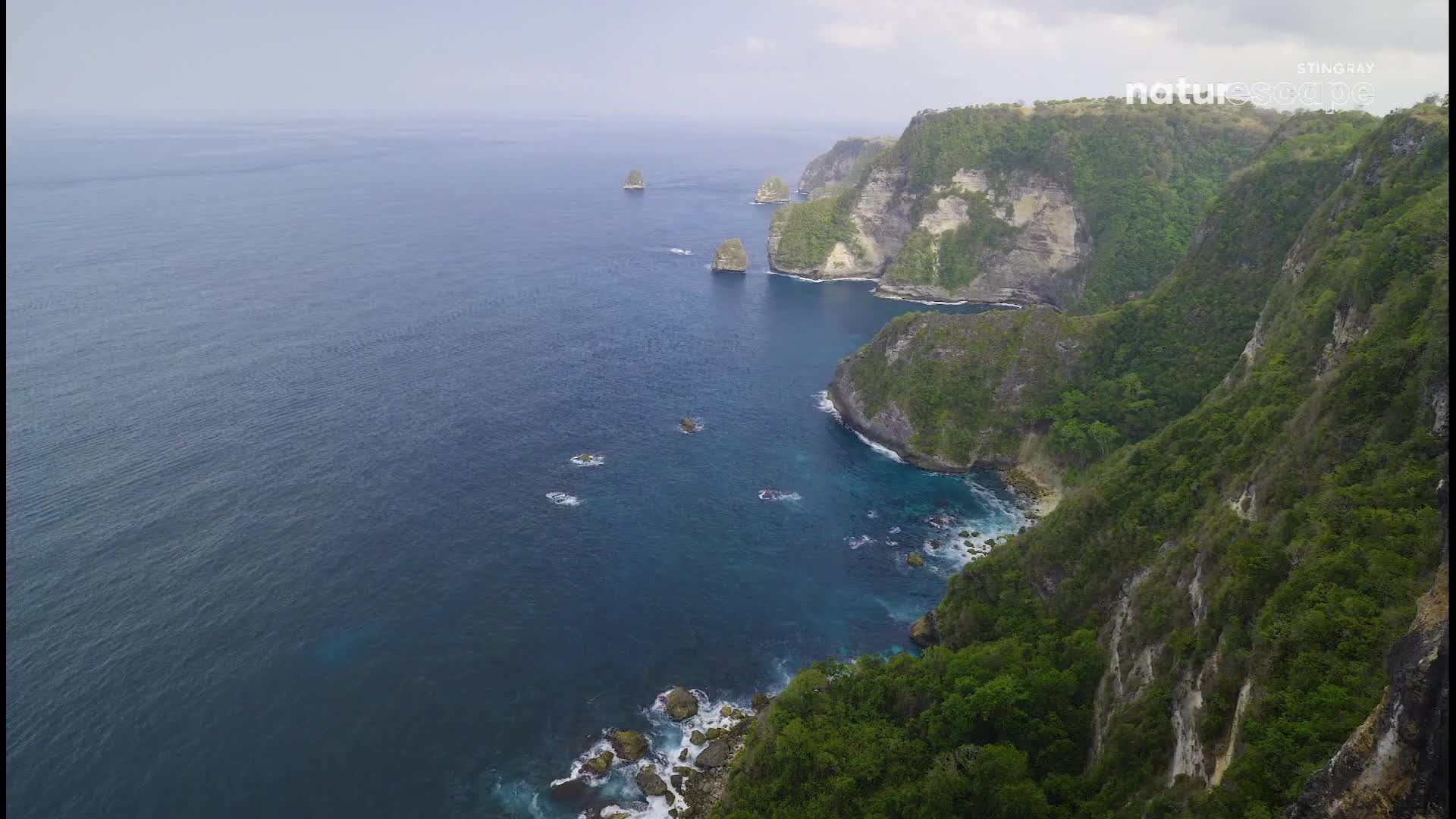 Several small boats navigate the deep blue water along a rugged, green coastline. The waves crash against the rocky shore, creating white foam. Several small boats navigate the deep blue water along a rugged, green coastline. The waves crash against the rocky shore, creating white foam.