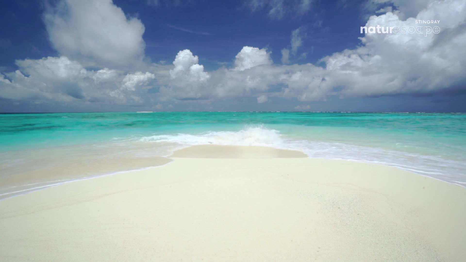 The turquoise water laps at the bright white sand.  Clouds drift across a brilliant blue sky over the ocean.