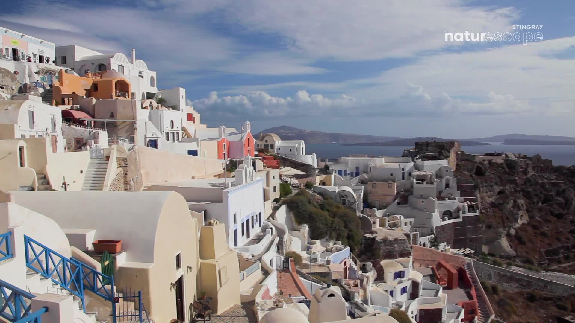White buildings cascade down the hillside towards the sea. A small pink church stands out against the whitewashed architecture.
