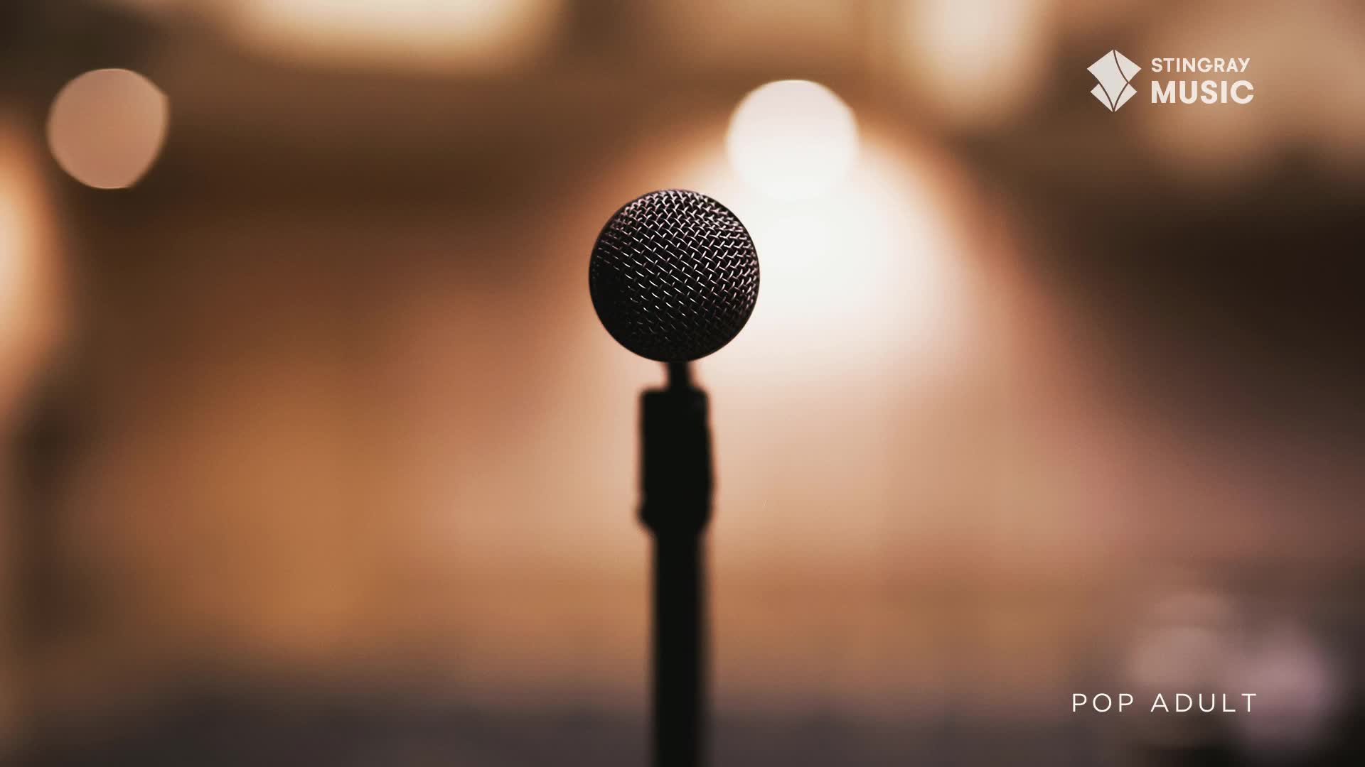 A microphone stands centered, its dark mesh head catching the light. Behind it, a warm, blurred background suggests a stage, perhaps for a Stingray Pop Adult show in Canada.
