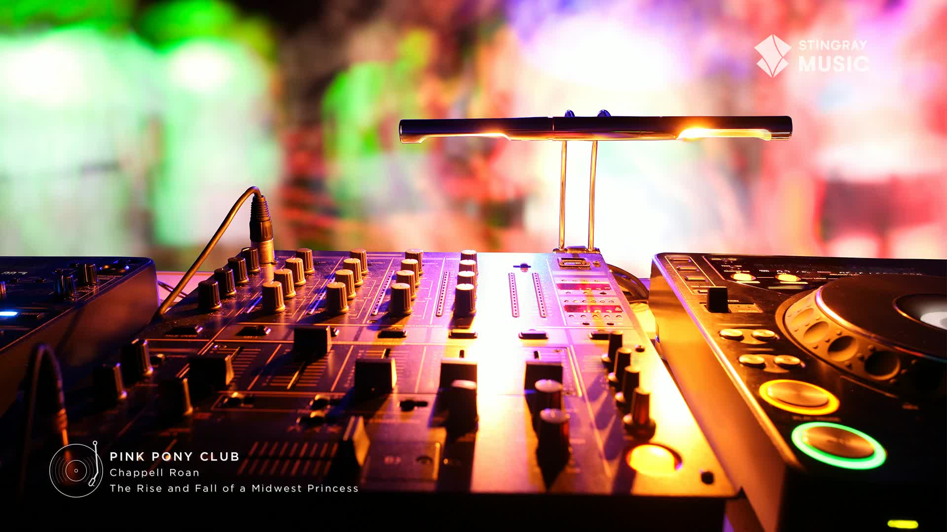 The DJ's mixer is lit up, with a warm glow highlighting the knobs and faders. Behind the equipment, a crowd is indistinct, bathed in colorful lights, as the Stingray Pop Adult music plays.
