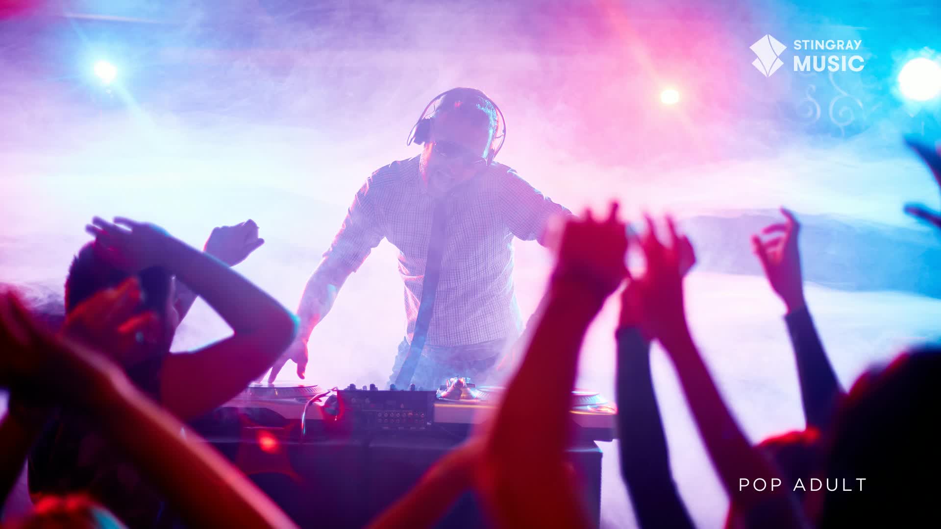The DJ, bathed in pink and blue light, stands hunched over his equipment, headphones on. Arms are raised in the crowd, reaching towards the stage, caught in the haze of a Stingray Pop Adult event in Canada.
