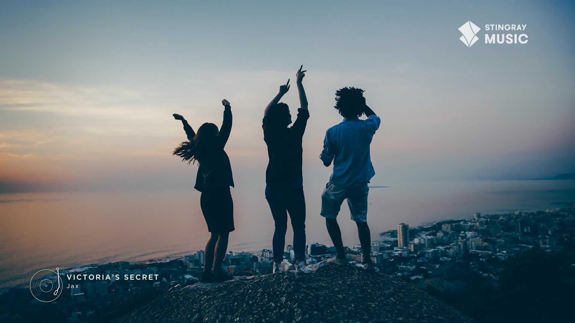 Three figures stand silhouetted on a hilltop, arms raised and dancing against a dusky sky. The city lights twinkle below, while the music of "Victoria's Secret" by Jax on Stingray Pop Adult in Canada fills the air.
