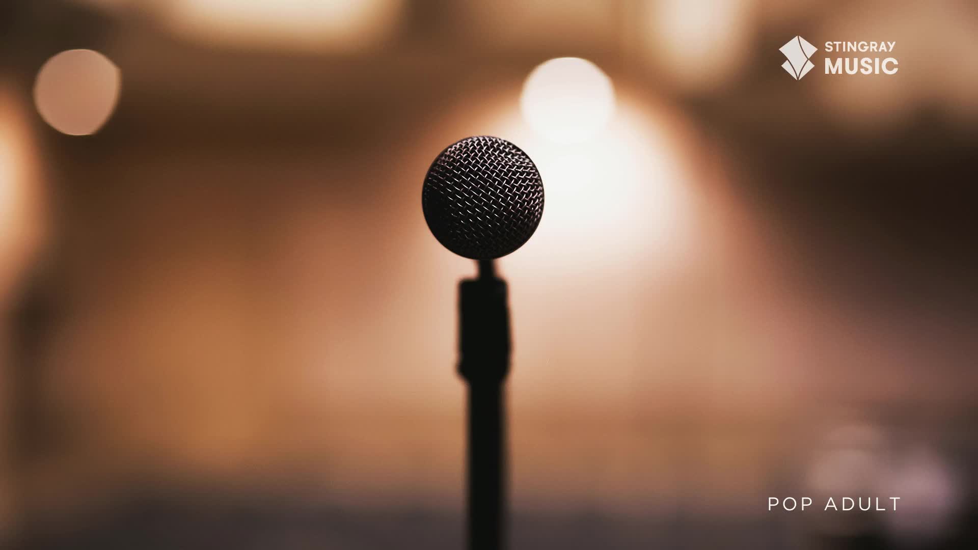 A microphone stands alone, silhouetted against a warm, blurred background, the Stingray Music logo in the corner. The stage is set for a performance on Stingray Pop Adult, somewhere in Canada.
