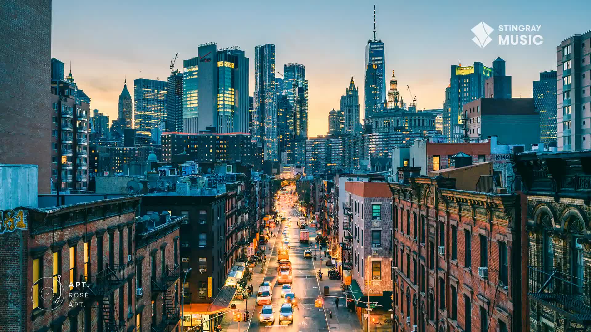 The city is waking up, the sky a soft gradient behind the towering skyscrapers. Cars crawl along the street below, their headlights illuminating the road as they head towards the horizon.
