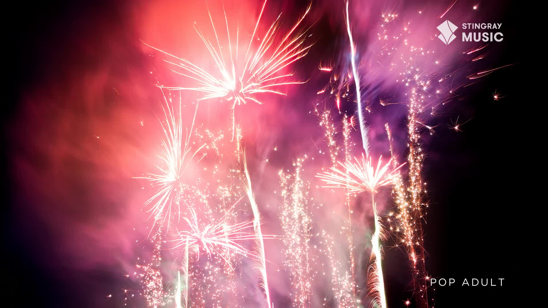 Explosions of pink and white light burst across the dark sky, trailing sparks like a shower of embers. The air is thick with smoke, catching the glow from the fireworks as they bloom overhead.