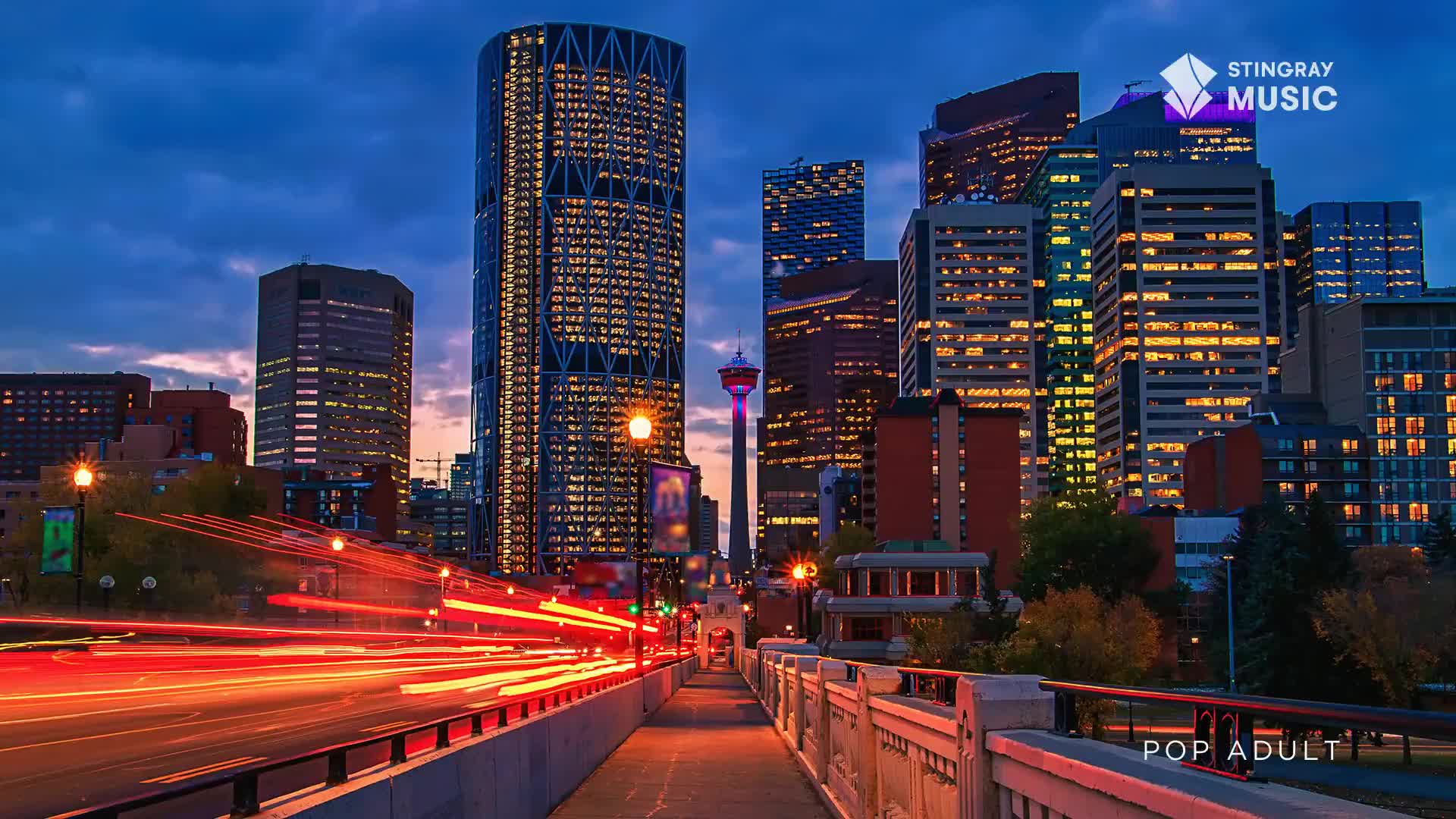 Headlights streak across the bridge as the city lights up for the evening. The Calgary Tower stands tall against the darkening sky.