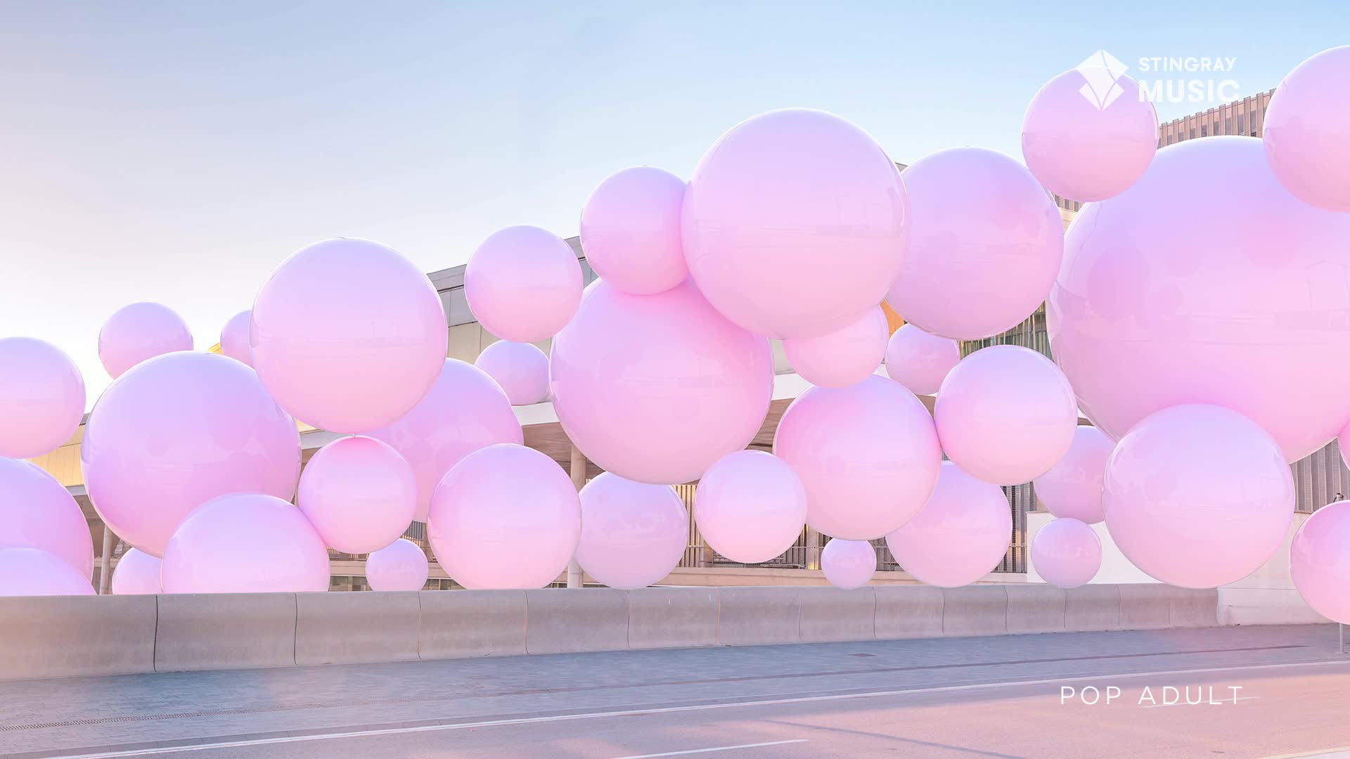 Giant pink spheres drift above a street in Canada, catching the soft afternoon light. A faint "POP ADULT" label appears near the bottom right.