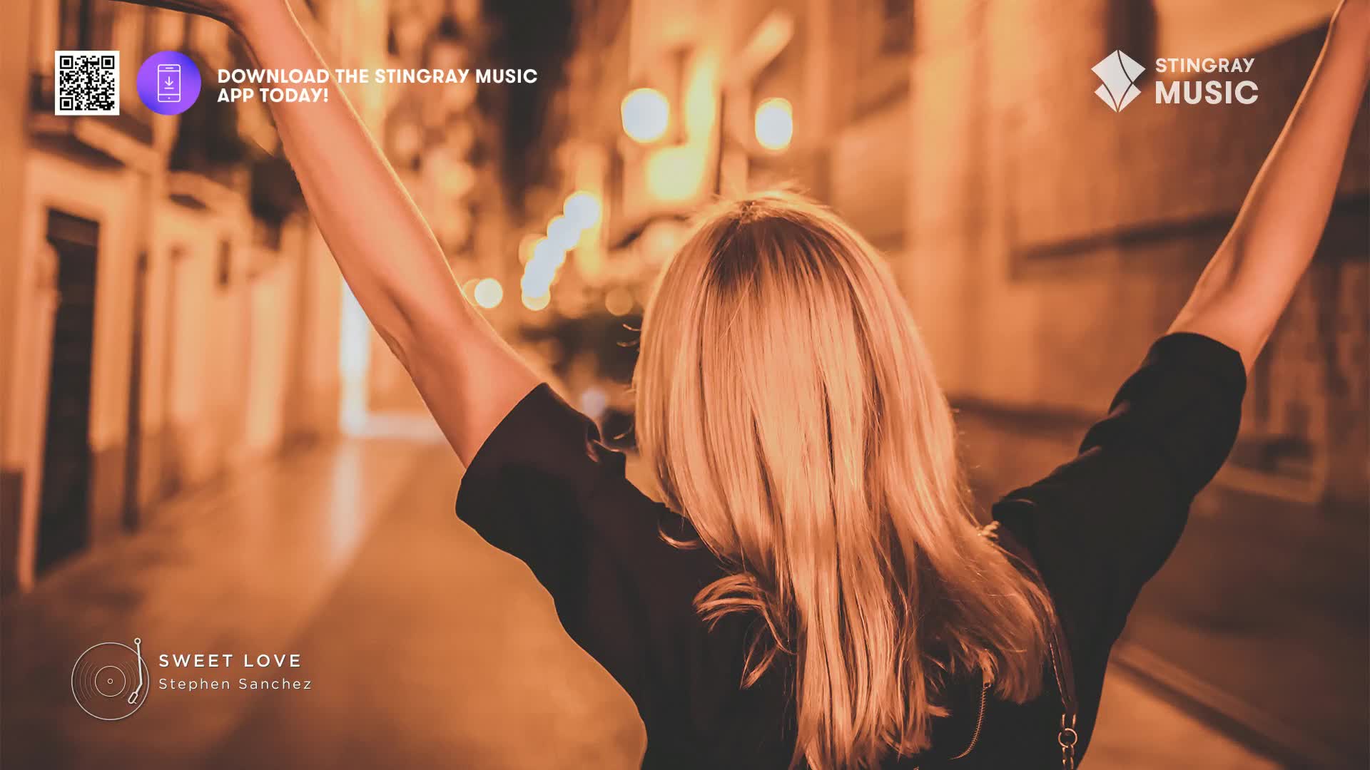 The streetlights cast a warm glow on the cobblestone path as a woman throws her arms up in celebration. Her blonde hair catches the light as she turns away, a smile I can only imagine on her face.