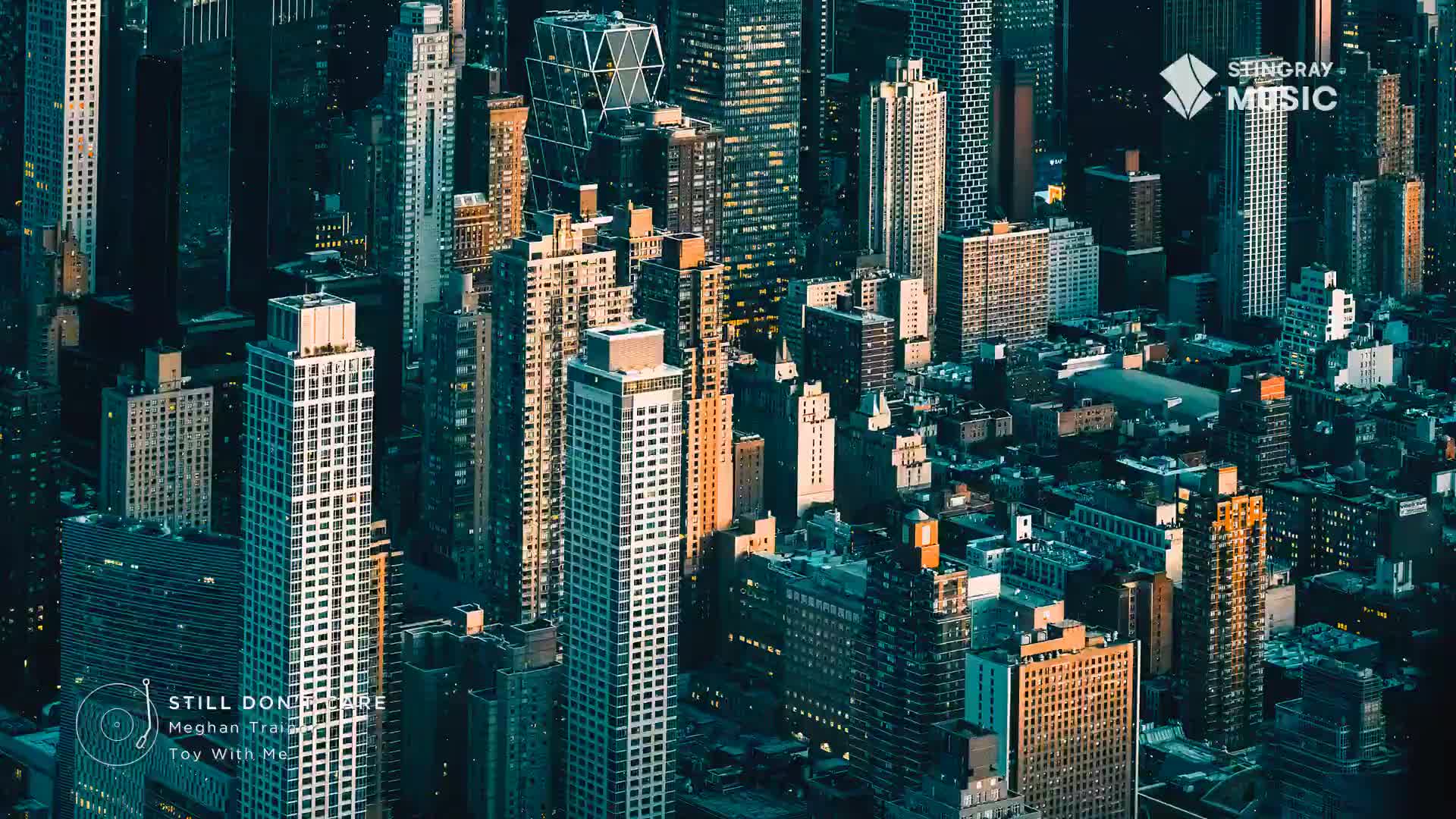 Sunlight catches the upper floors of skyscrapers, casting long shadows over the dense urban landscape. The Stingray Music logo appears on a tall building, a subtle reminder of the pop adult soundtrack playing. Sunlight catches the upper floors of skyscrapers, casting long shadows over the dense urban landscape. The Stingray Music logo appears on a tall building, a subtle reminder of the pop adult soundtrack playing.