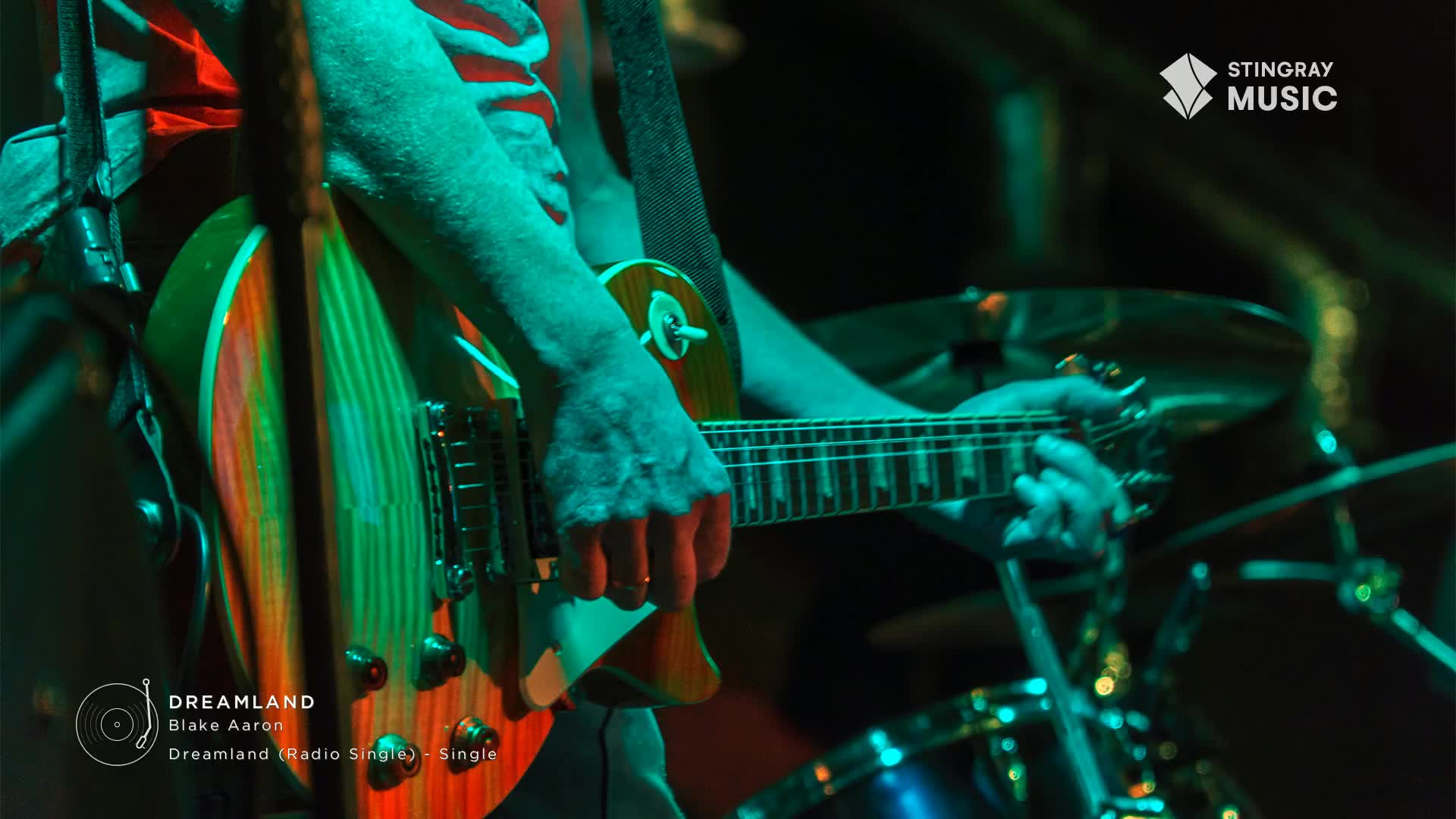The musician's fingers dance across the fretboard of a sunburst guitar, illuminated by the green stage lights. The music, a smooth jazz track from Blake Aaron, fills the air, courtesy of Stingray Music in Canada.
