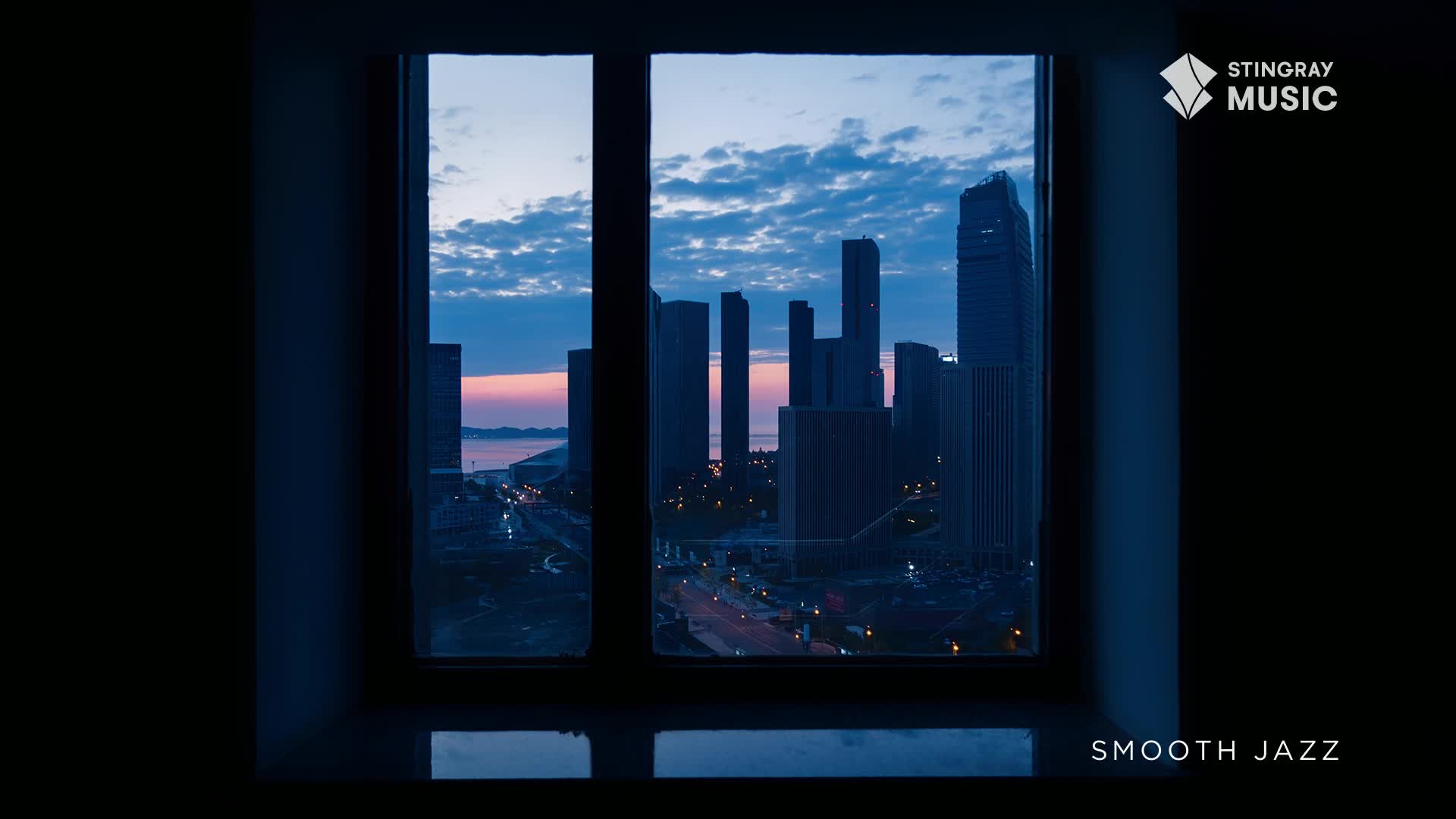 Through the window, the city's silhouette is stark against a sky streaked with pink and blue. Below, the lights of the city are starting to come on, and the whole scene feels like the perfect backdrop for Stingray Smooth Jazz.
