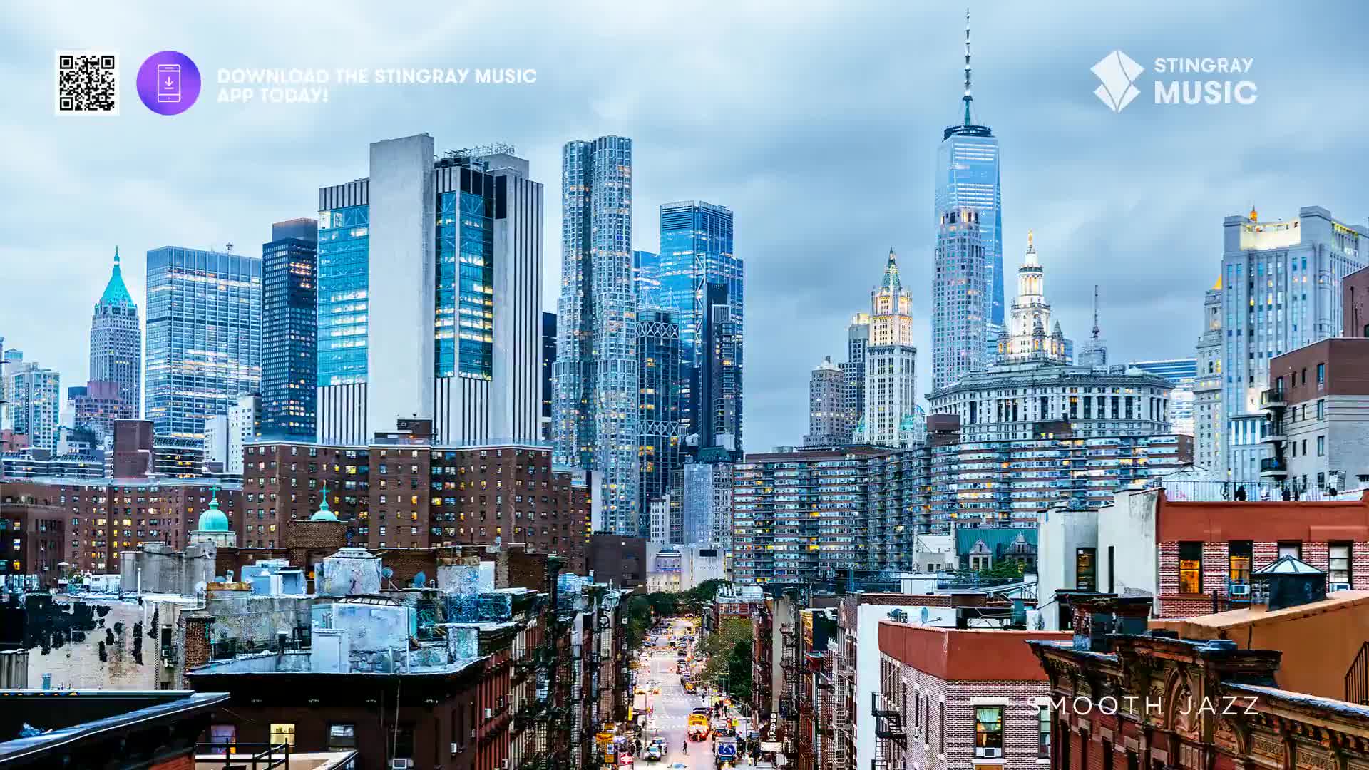 The city's skyline rises in a dense cluster of towers, the tallest piercing the overcast sky. Below, a long street stretches into the distance, its lights twinkling like a trail of gold as the city hums with activity, maybe a Stingray Smooth Jazz playlist playing in the background.
