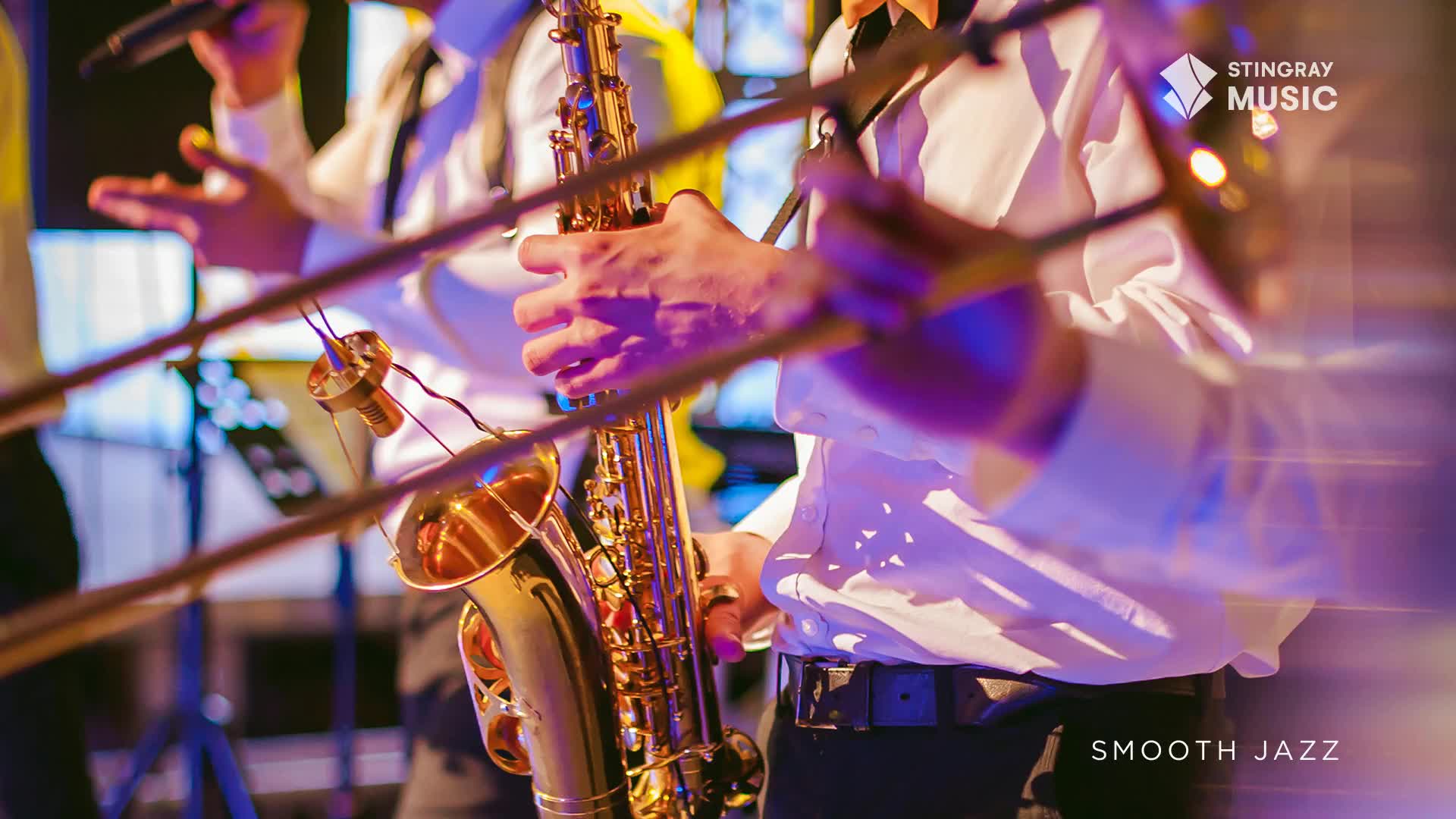 A saxophone gleams under stage lights, held by a musician in a crisp white shirt. The band is playing, part of a Stingray Smooth Jazz performance, and the music is flowing.
