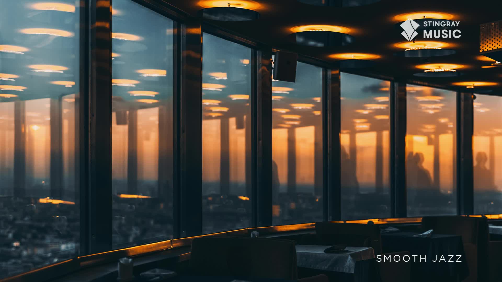The city lights are dimming outside, reflecting in the tall windows of this Canadian restaurant. Soft, warm light from the ceiling fixtures illuminates the tables, while the Stingray Smooth Jazz logo sits in the corner.
