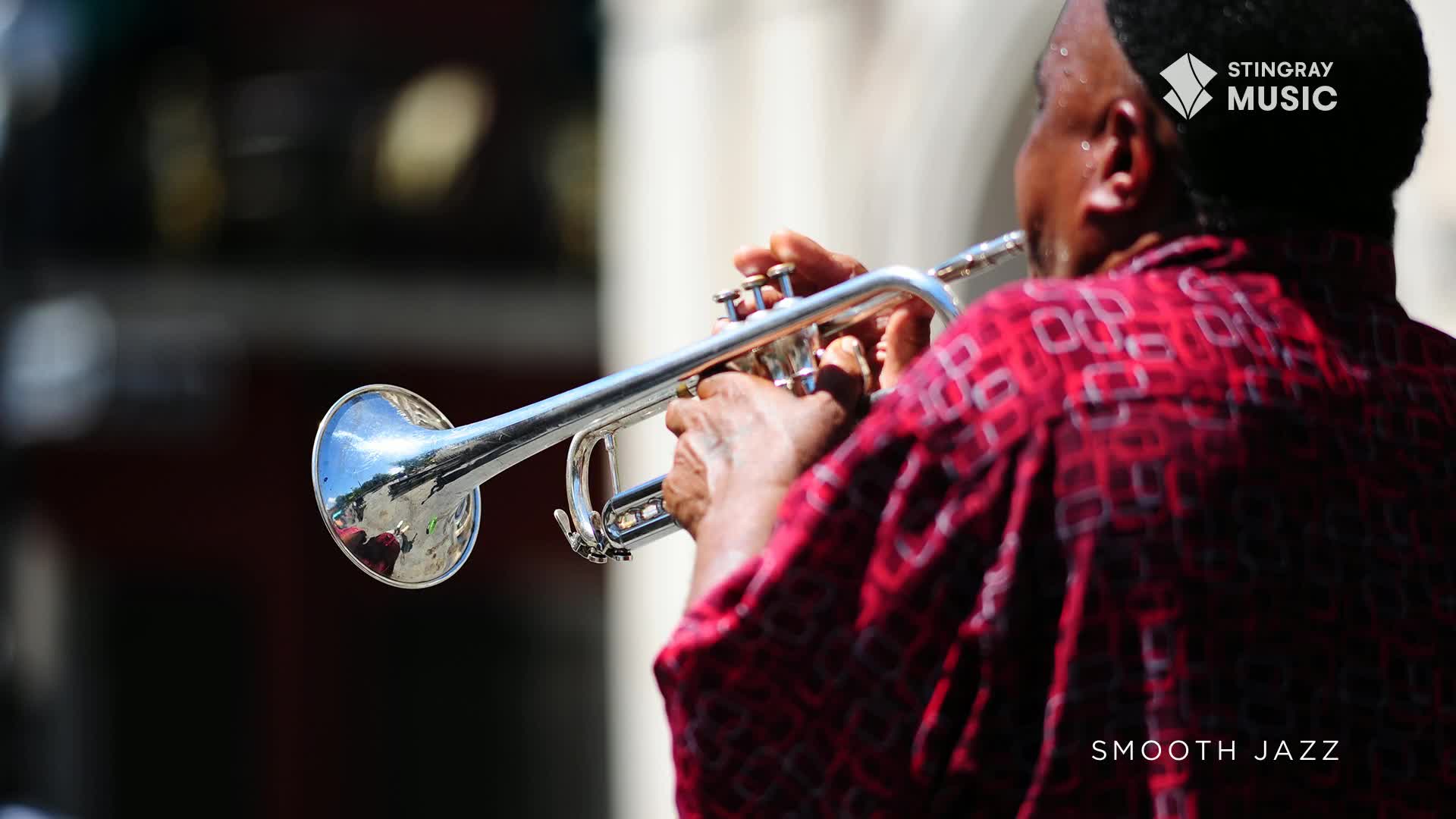 A musician in a red shirt holds a gleaming trumpet, its bell reflecting the sun. His fingers dance over the valves as he plays, likely a smooth jazz tune, a sound you'd expect to hear on Stingray Music in Canada.
