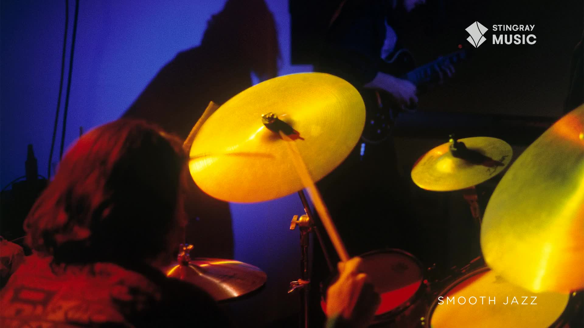 The drummer's sticks hit the cymbals, sending bright yellow flashes across the stage. A guitarist's silhouette and the Stingray Smooth Jazz logo hint at the music's Canadian roots.
