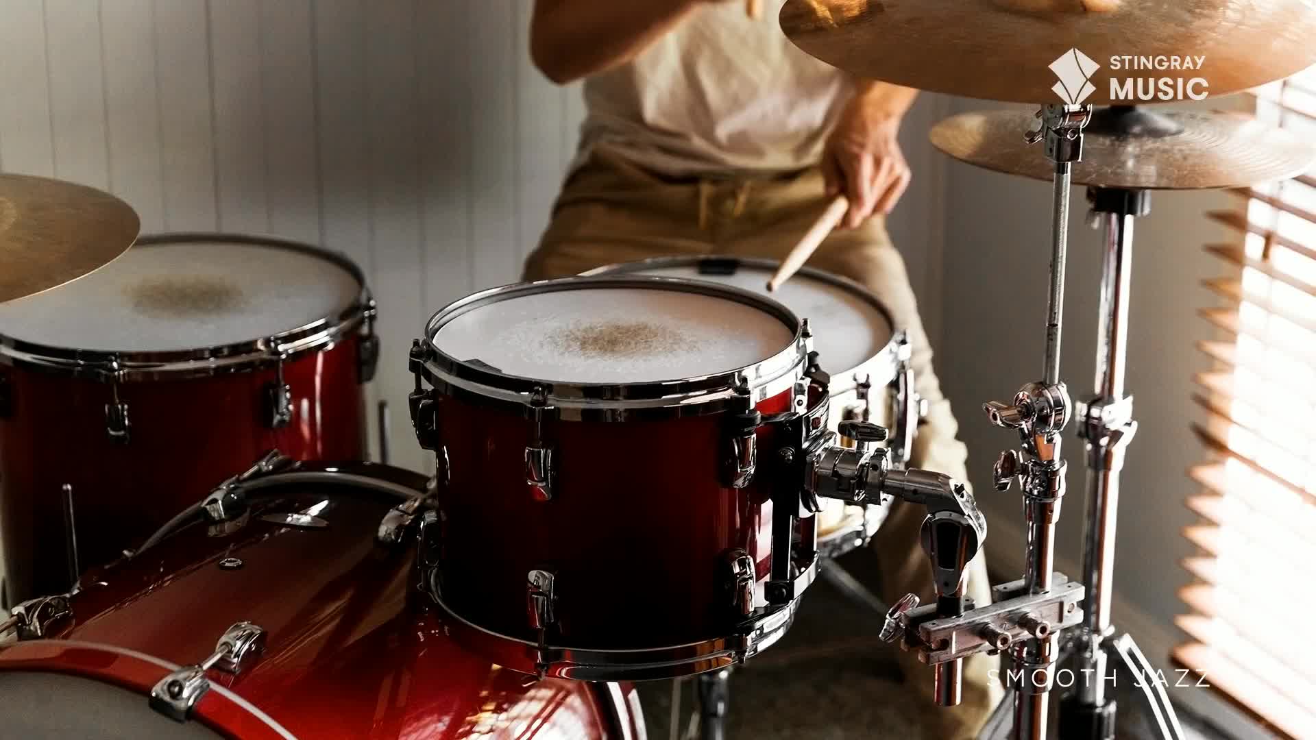 Drumsticks strike the snare, a steady rhythm for this Canadian smooth jazz track. The shiny red drums gleam under the studio lights.