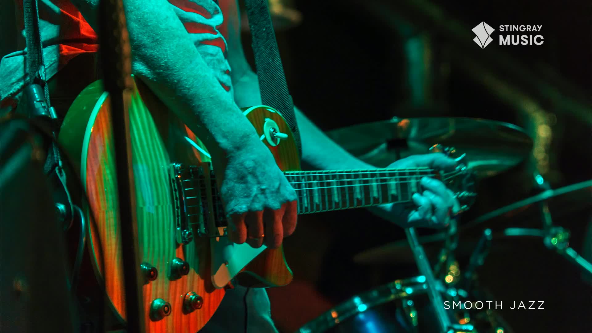 The guitarist's fingers dance across the fretboard of a sunburst electric guitar, bathed in cool green stage lights. The vibrant stripes of the guitar's body catch the light, a beautiful contrast to the dark backdrop of the Canadian venue.