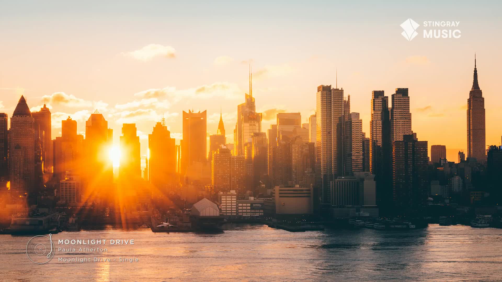 The sun is setting, casting a warm glow over the city skyline. A few boats are visible on the water in front of the buildings. The sun is setting, casting a warm glow over the city skyline. A few boats are visible on the water in front of the buildings.
