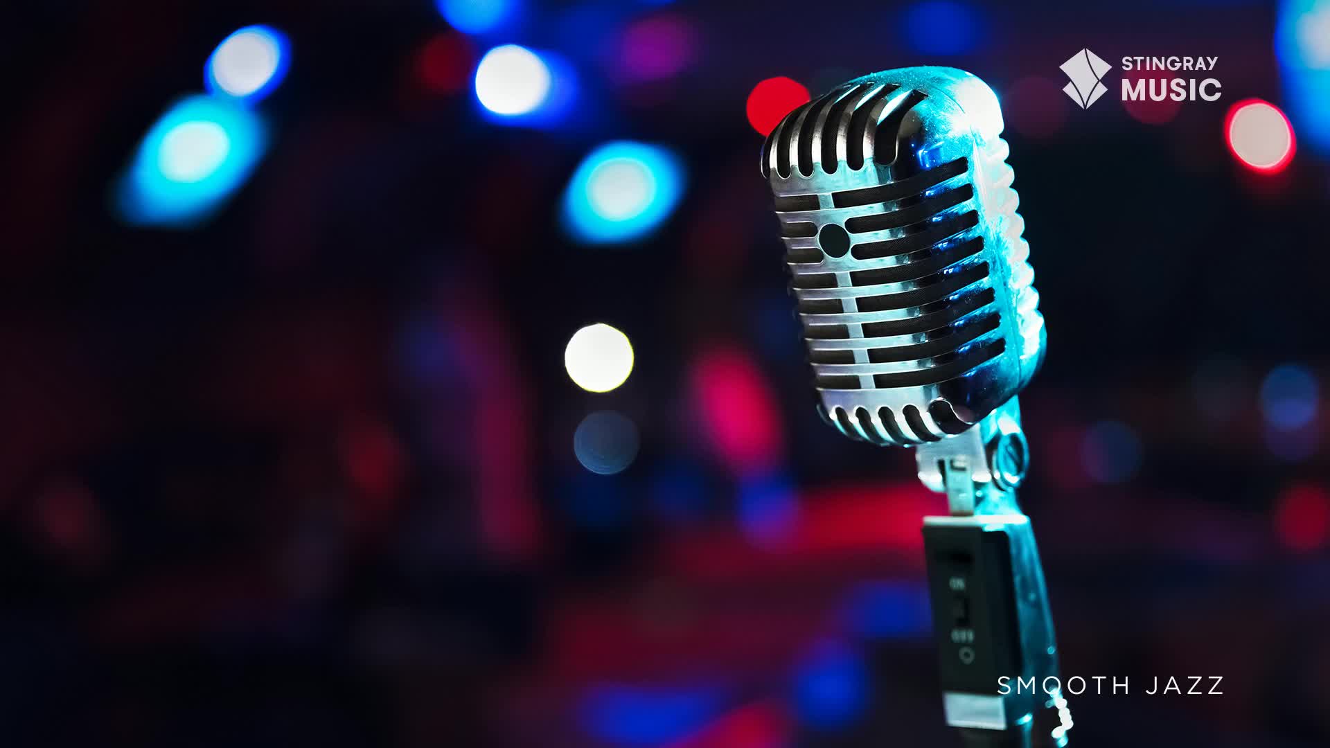 A vintage microphone stands ready on a stage, bathed in the soft glow of blue and red lights. This is the setup for a Stingray Smooth Jazz performance.