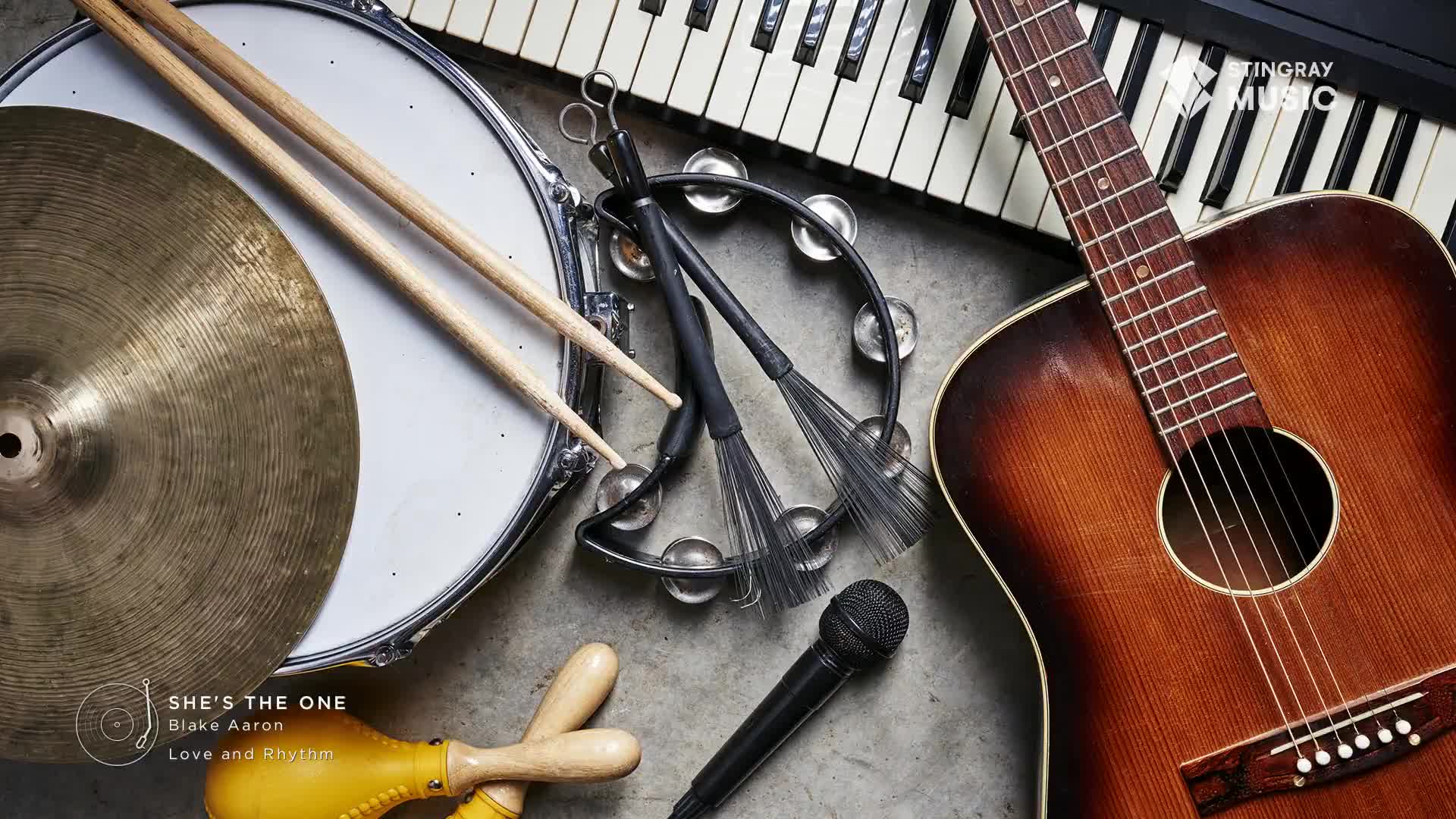 Acoustic guitar, snare drum, and keyboard sit ready for a Stingray Smooth Jazz session. Maracas and a microphone complete the setup for Blake Aaron's "She's the One."