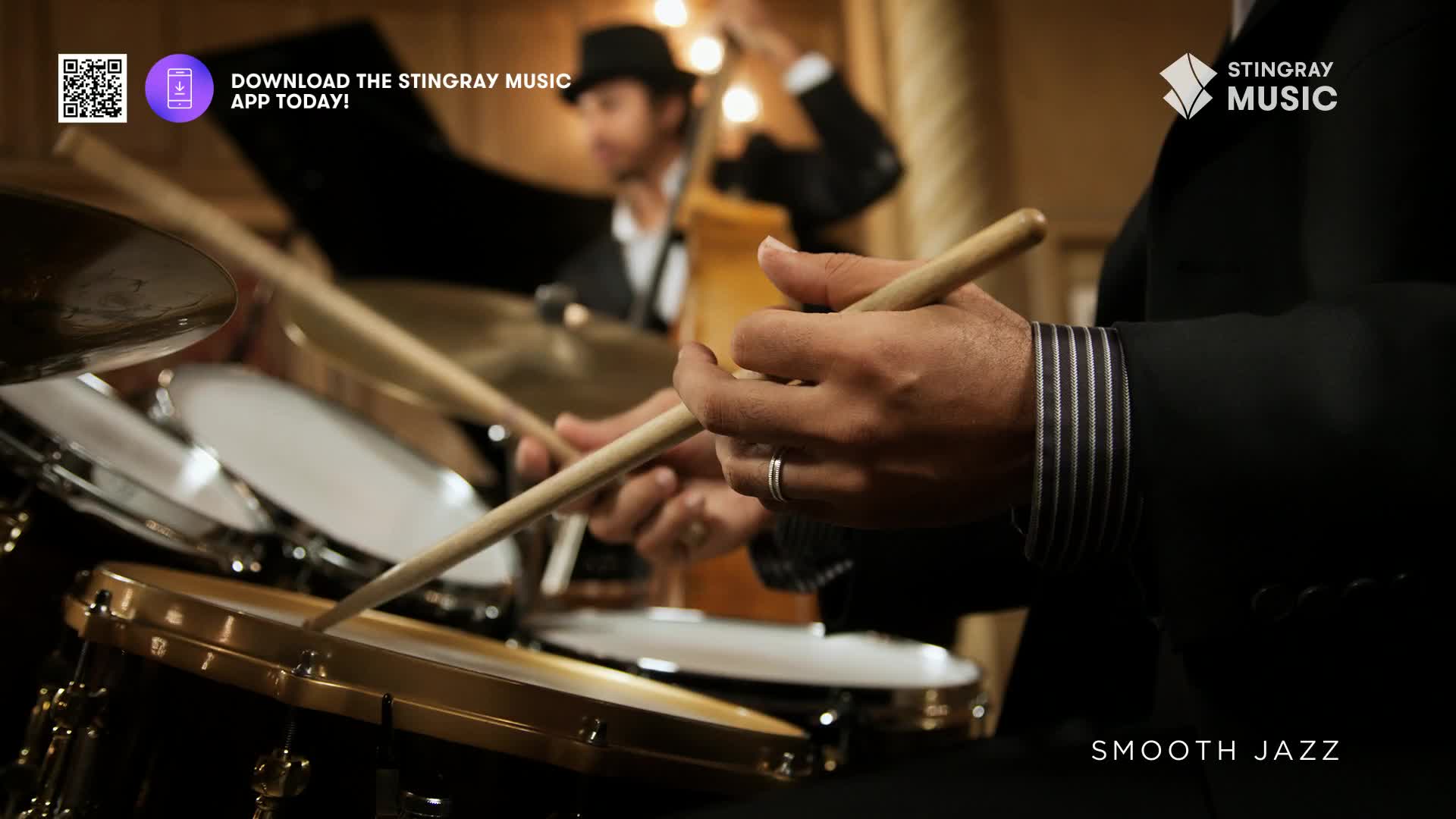 Drumsticks dance across the snare, a steady rhythm building. Behind, a bassist stands, his instrument poised for the next phrase of smooth jazz.