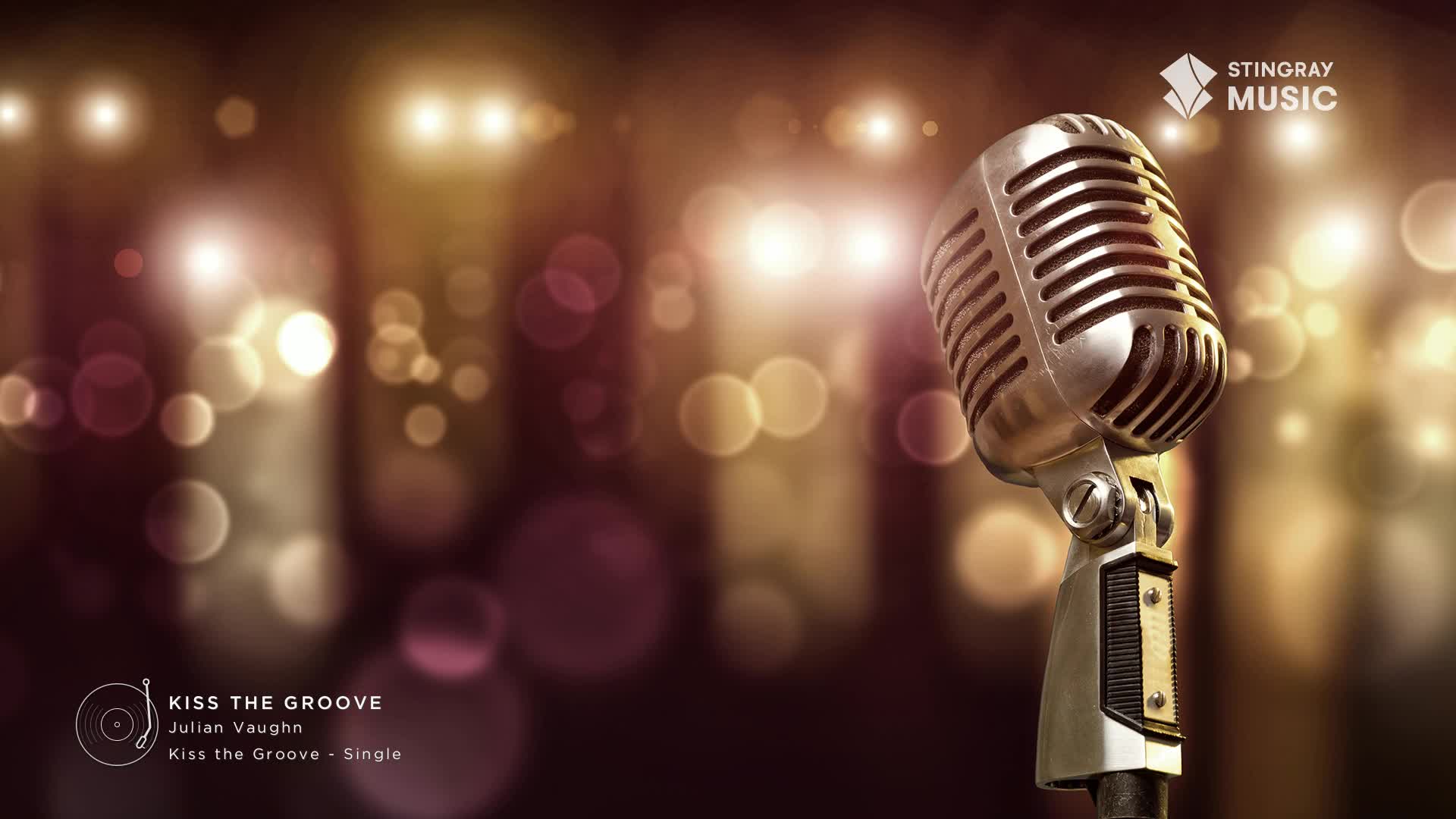 A vintage microphone stands center stage, bathed in the warm glow of stage lights. This is for Julian Vaughn's single, "Kiss the Groove," playing on Stingray Smooth Jazz.