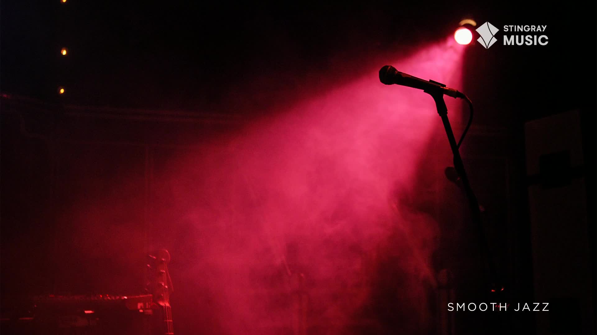 A single microphone stands ready on stage, bathed in a vibrant pink spotlight that cuts through the smoky air. This is the calm before the music starts, a moment of anticipation for a Stingray Smooth Jazz performance in Canada.