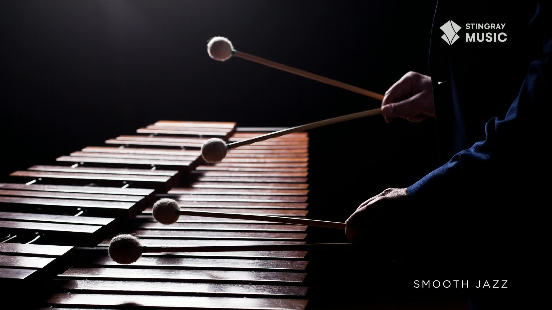 Mallets strike the wooden bars of a marimba, creating a rich sound. The smooth jazz melody fills the air as the musician's hands move with practiced grace.