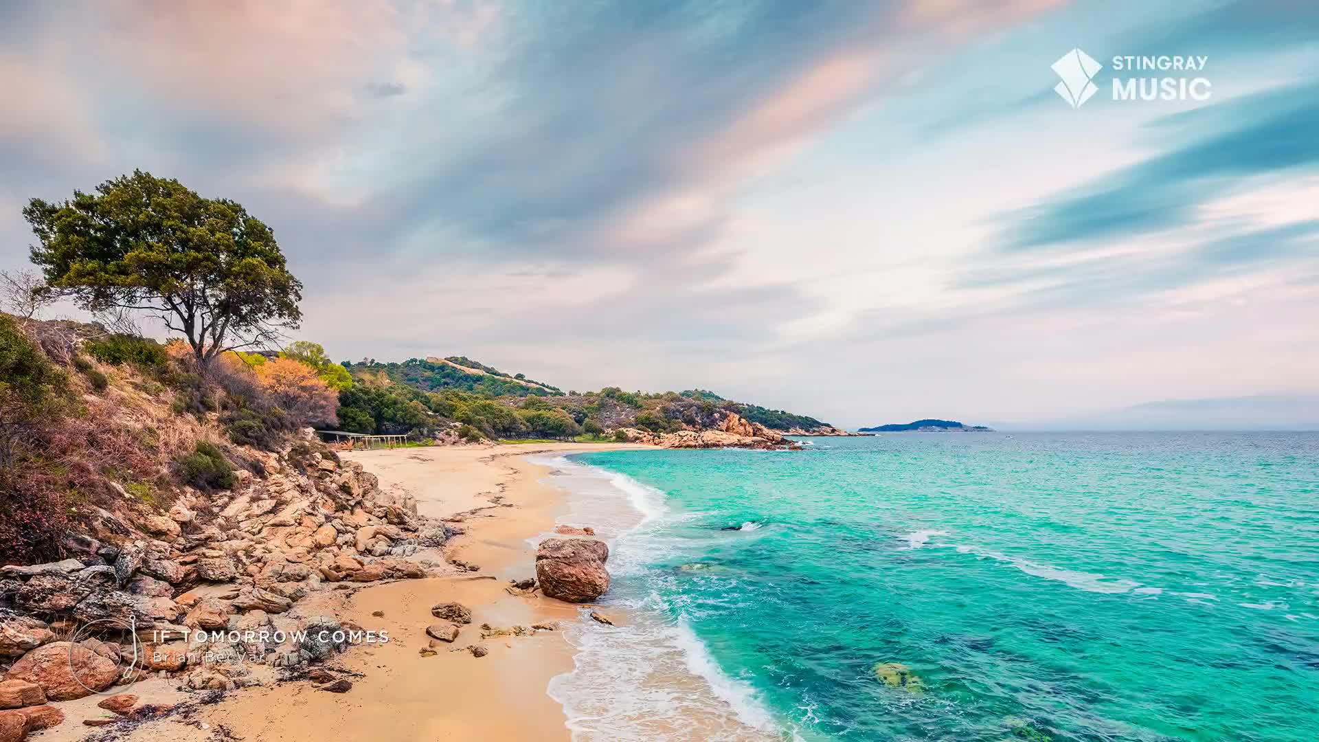The turquoise water laps gently onto a sandy beach, framed by a rocky outcrop and a lone, windswept tree. Above, a sky of soft pinks and blues promises a peaceful day, perfect for unwinding at Stingray The Spa.
