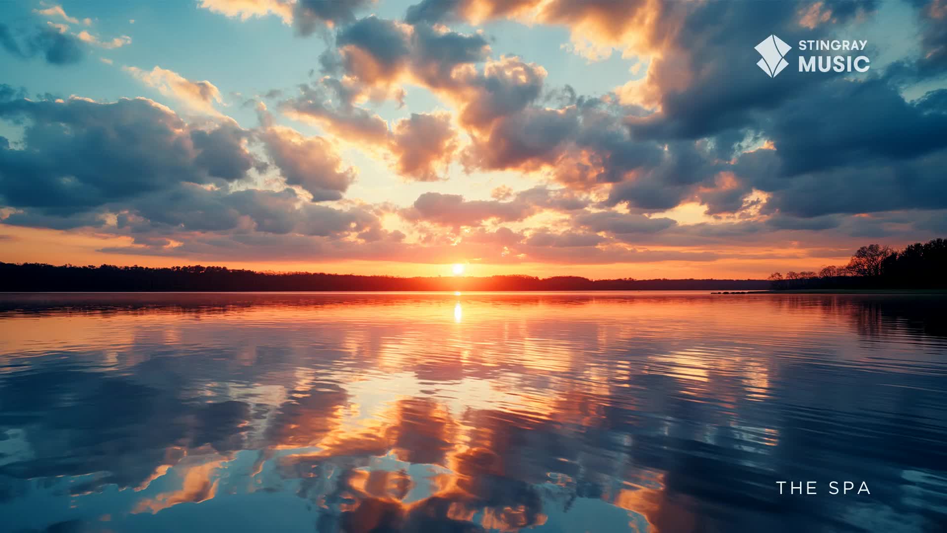 The sun bleeds orange across the lake, reflecting the sky's fiery hues. Dark clouds drift above, mirrored in the still water, creating a tranquil scene for Stingray The Spa.
