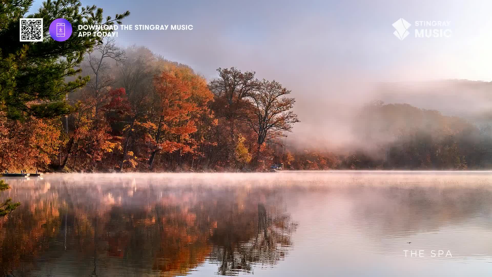 Mist hangs low over the still water, reflecting the vibrant autumn foliage along the Canadian shoreline. The air is crisp, and the scene feels peaceful, like a Stingray The Spa advertisement come to life.

