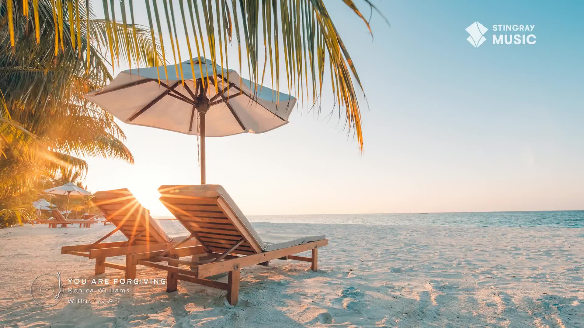 The sun bursts through the umbrella, casting a warm glow on the empty lounge chairs. Palm fronds sway gently in the breeze as the ocean stretches out towards the horizon.
