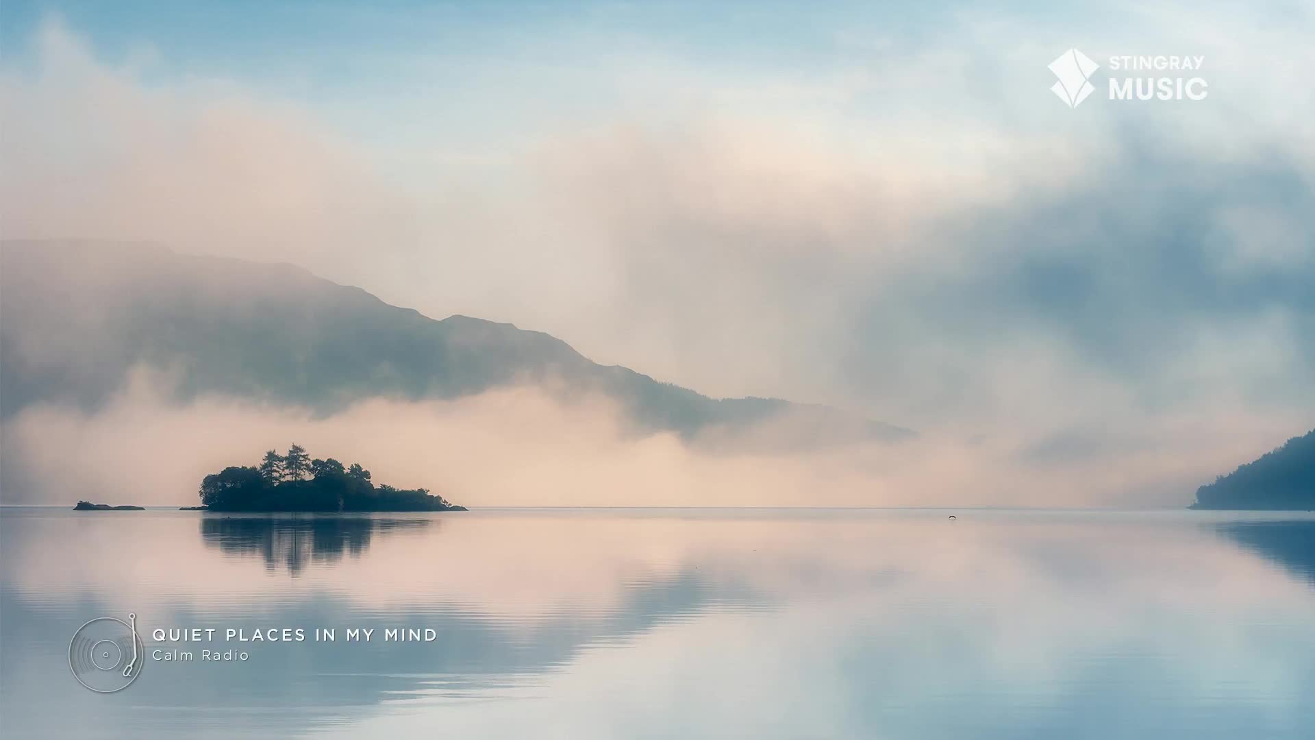 Mist drifts across the lake, softening the distant mountains and the small island's trees. The water mirrors the sky, creating a serene, almost dreamlike scene, perfect for a spa day in Canada.
