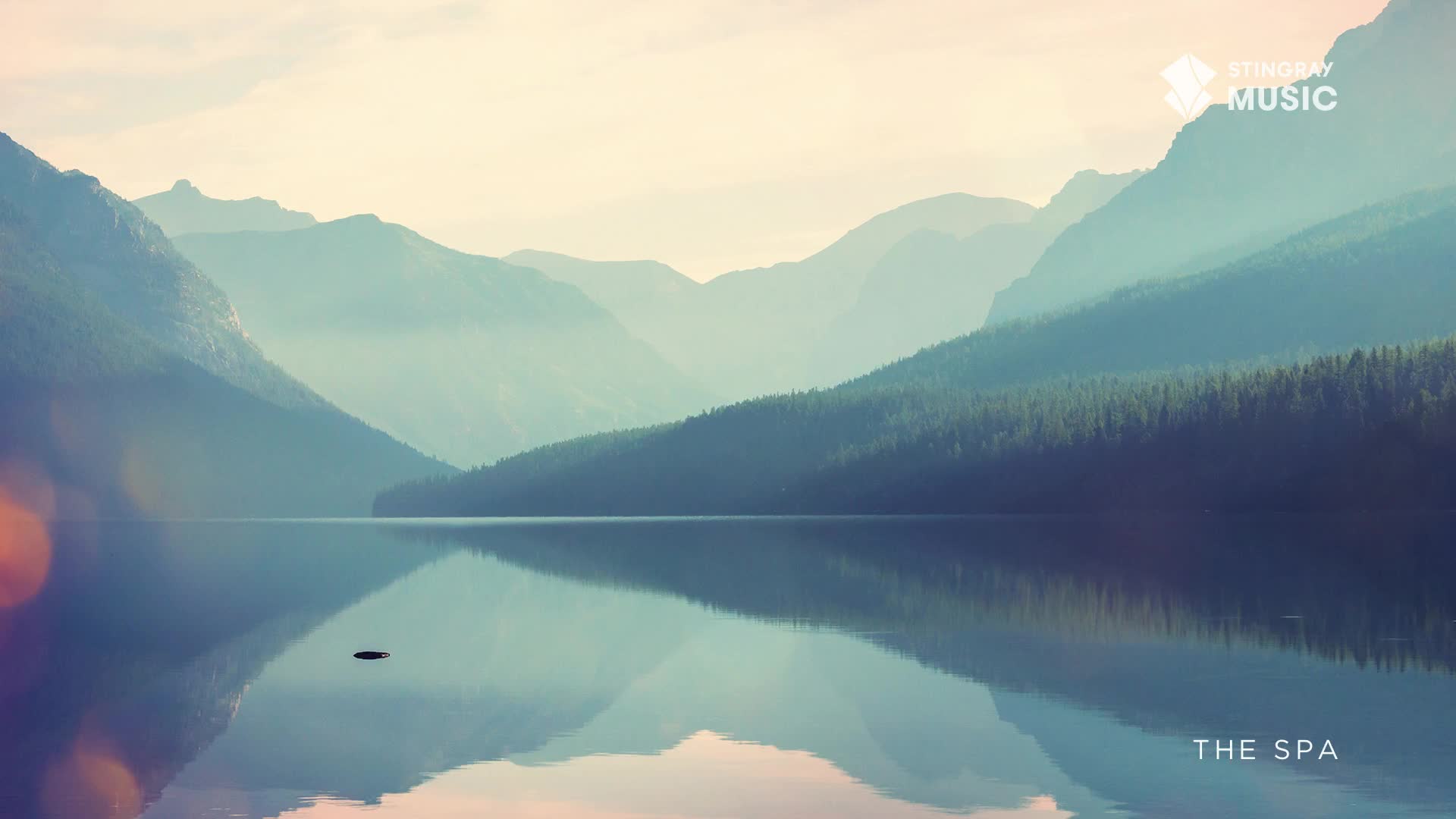 The calm water perfectly mirrors the hazy blue mountains and dark green forest. A small, dark object breaks the surface of the lake in the distance.