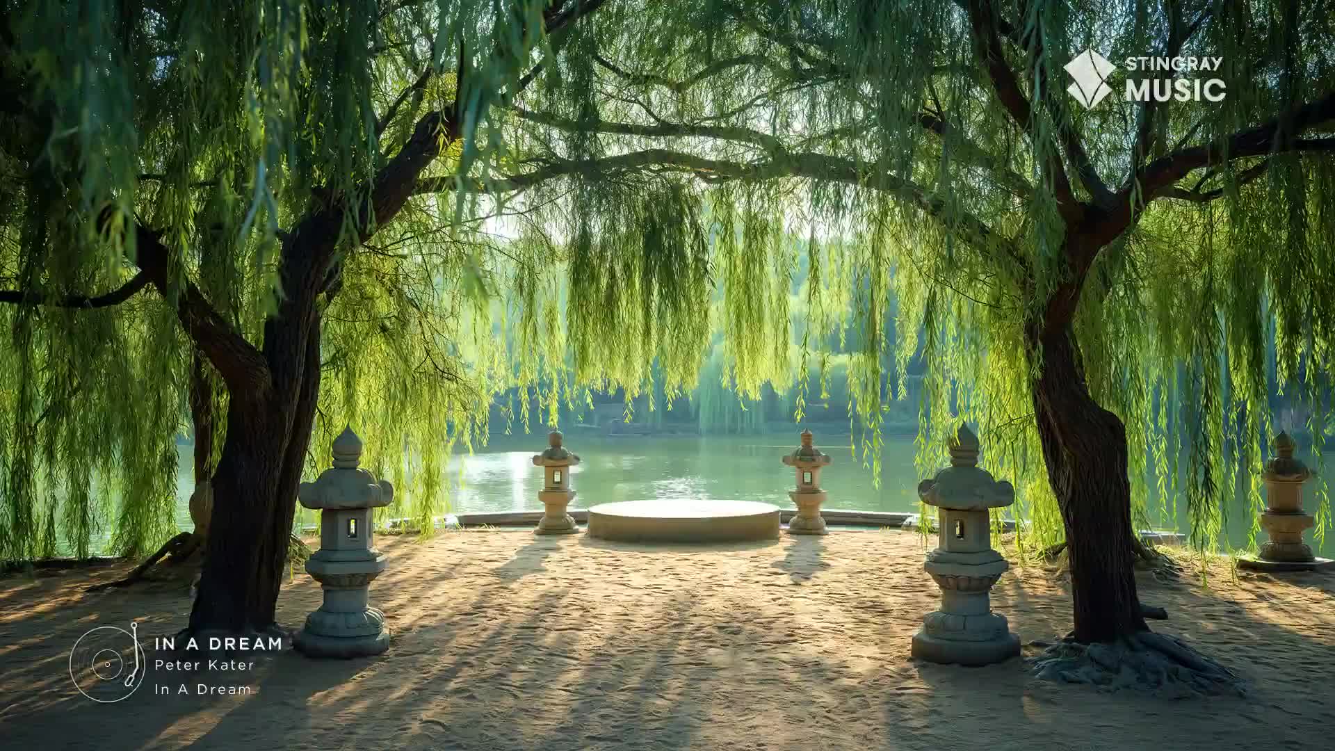 Sunlight filters through the weeping willow branches, dappling the sandy ground. Stone lanterns stand sentinel beside a circular platform overlooking a calm body of water.