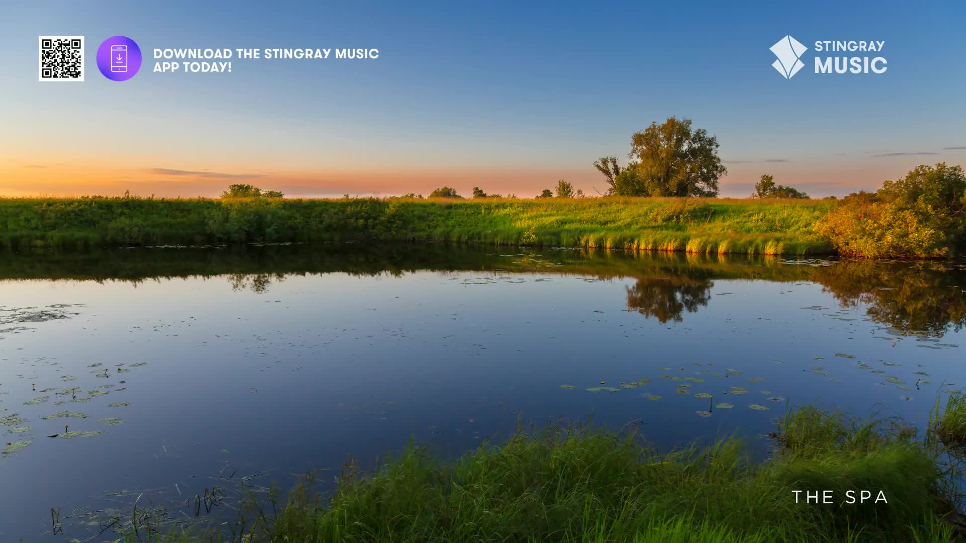 The sun dips low, casting a warm glow across the Canadian landscape. A calm river reflects the vibrant sky and the lush green banks, creating a peaceful scene.
