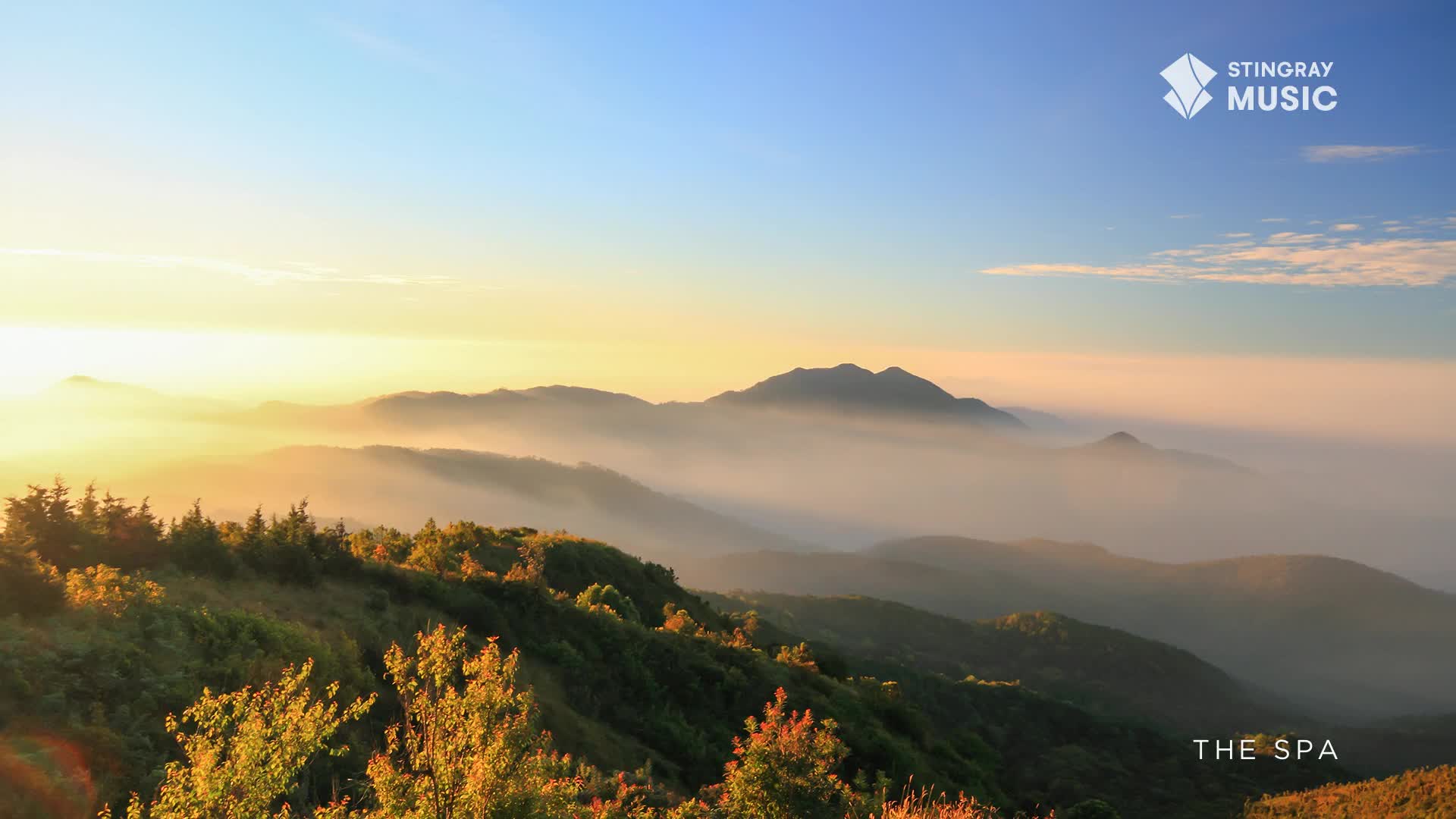 The sun breaks over distant Canadian peaks, painting the sky in soft yellows and blues. A gentle mist settles in the valleys below, creating layers of hazy mountains.