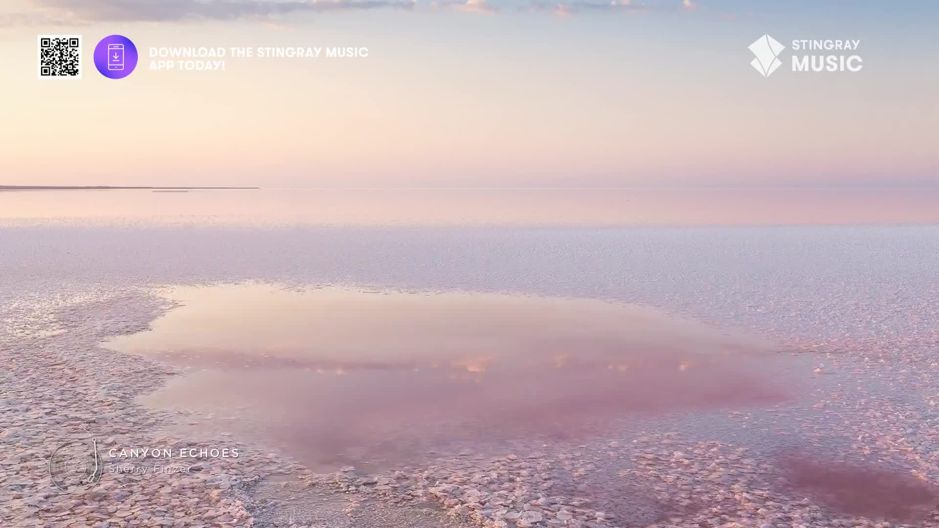 The vast, pink-tinged salt flats stretch out under a soft sky. A small pool of water reflects the pastel clouds, its edges fringed with salt crystals.