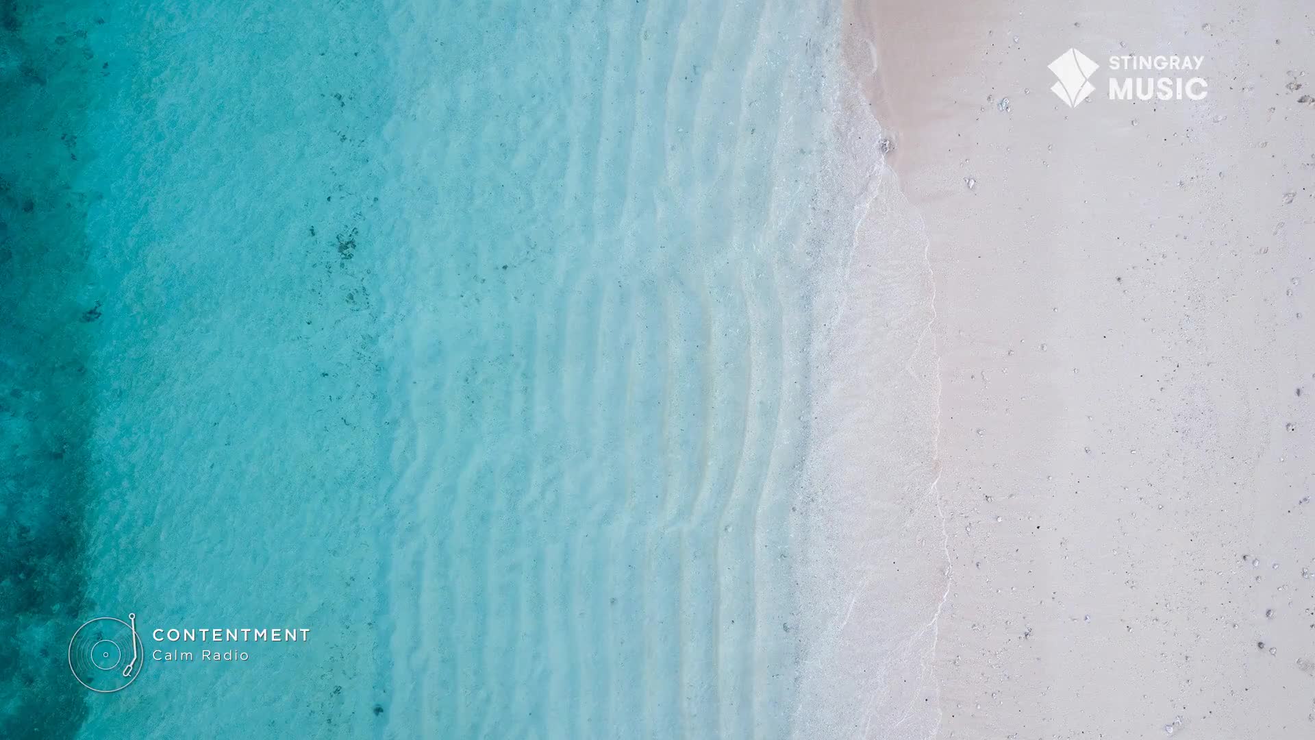 The shallow, clear water laps gently onto the pale sand. Ripples on the seabed create subtle patterns beneath the surface. The shallow, clear water laps gently onto the pale sand. Ripples on the seabed create subtle patterns beneath the surface.