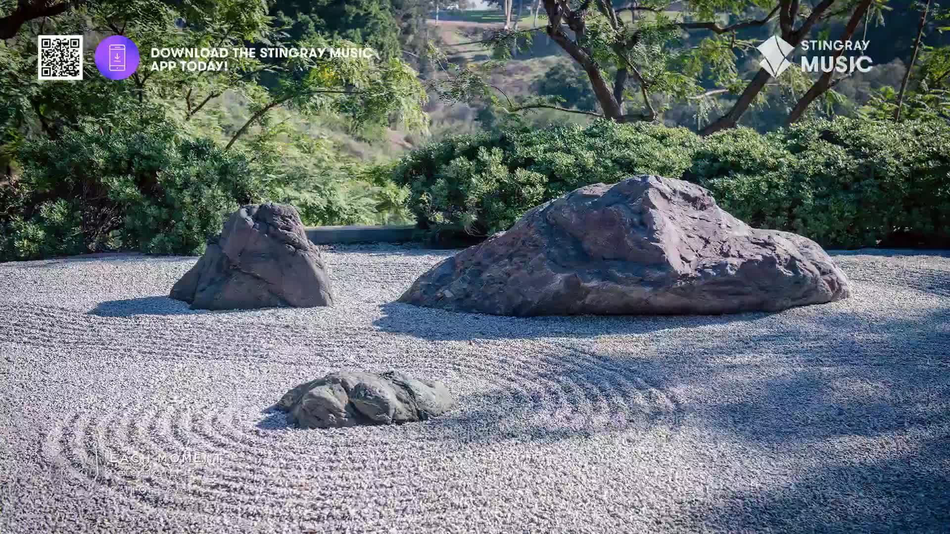 The raked gravel of a Japanese garden surrounds three large stones. Lush green foliage frames the scene, hinting at a tranquil spot like Stingray The Spa in Canada.