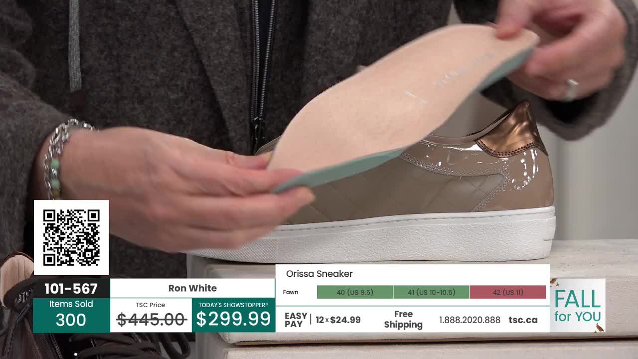 A person is holding a shoe's insole, showing it off next to the sneaker. The shiny, taupe-colored shoe sits on a white surface, ready for the insole to be placed inside.
