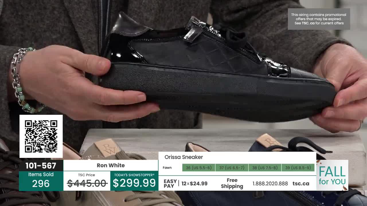 A person is holding up a black sneaker, showing off the details of the shoe. The TSC price is displayed on the screen, along with the brand and a QR code.
