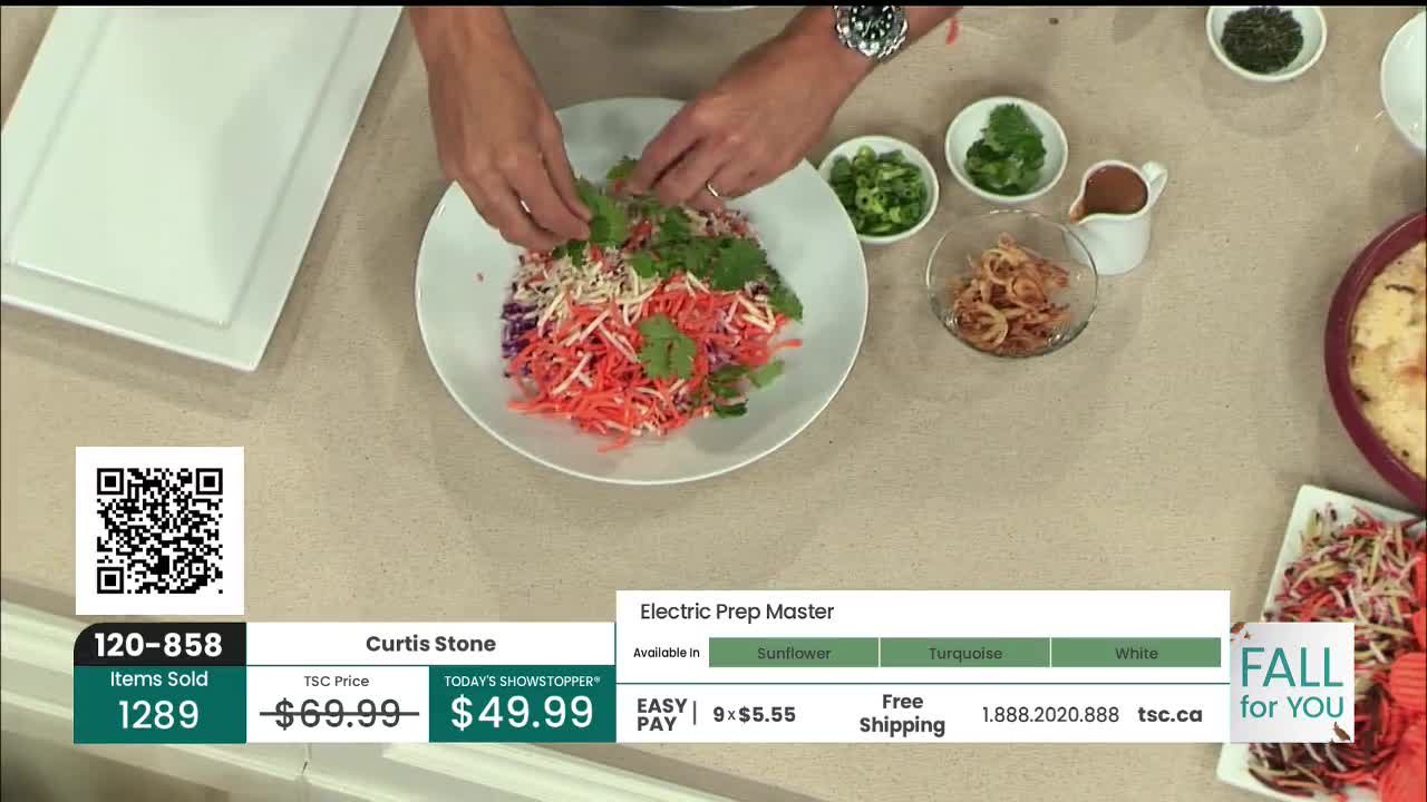 A man is arranging fresh herbs on top of a colorful salad. The scene is set on a countertop, with various ingredients and a small dish of sauce nearby.
