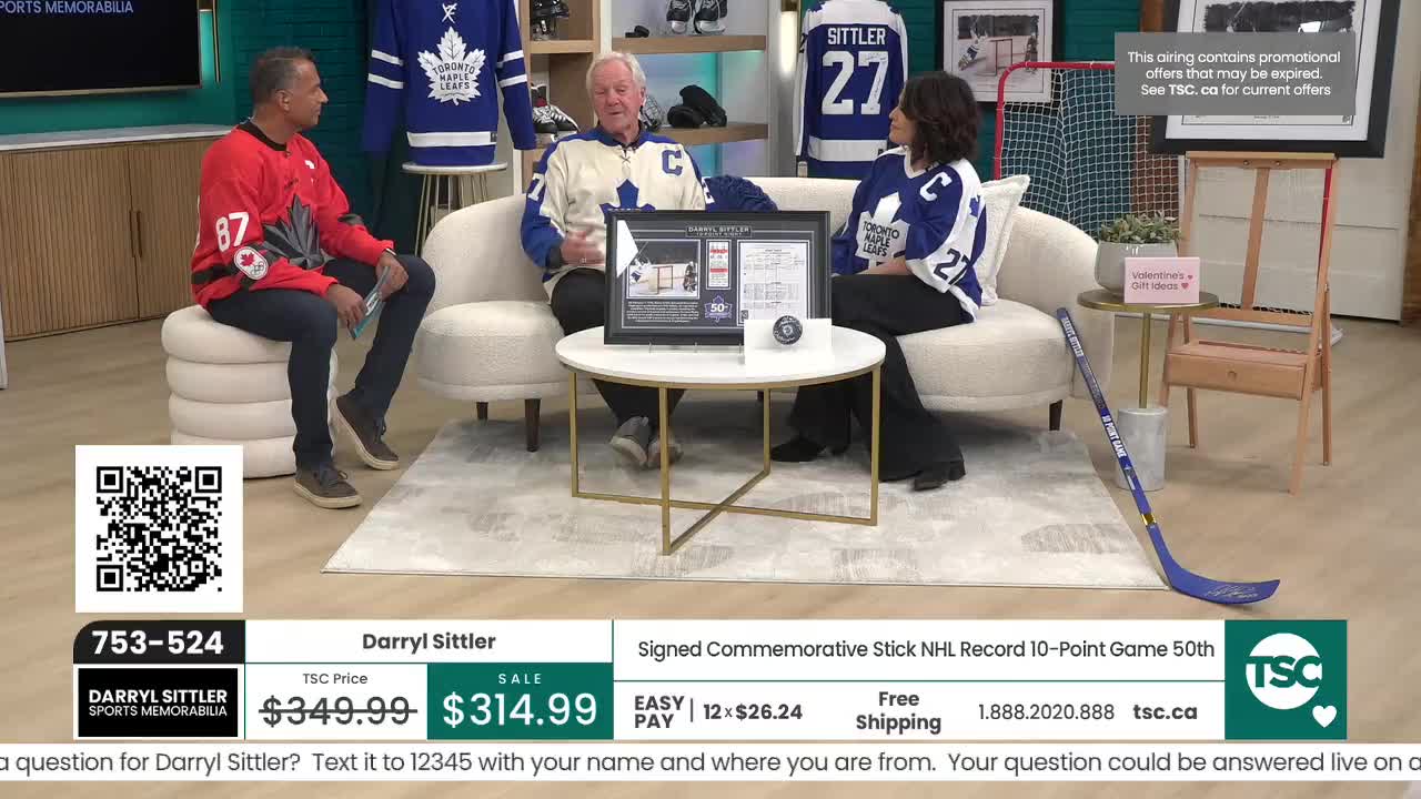 A man in a red jersey sits to the left of a couple on a couch, all three are in a studio setting. A framed hockey collectible rests on a coffee table between them.