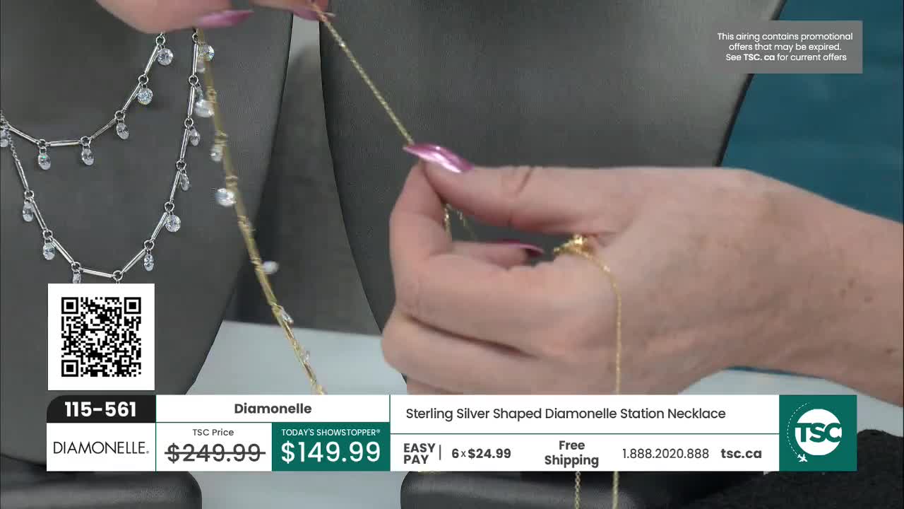 Fingers with pink polish adjust a delicate gold chain necklace. Another silver necklace with dangling clear stones rests on a dark display.