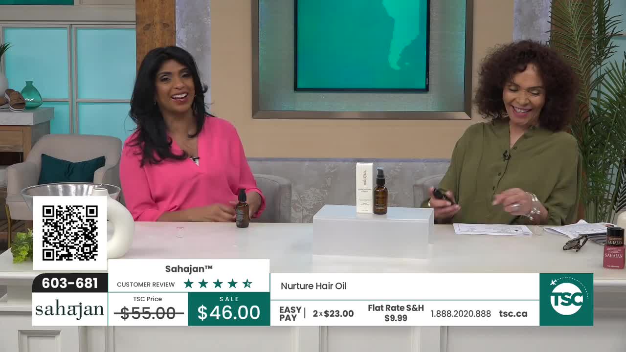 Two women are on a set, presenting a product. One woman in a pink top smiles, holding a small bottle. The other, in an olive green shirt, examines a piece of paper.