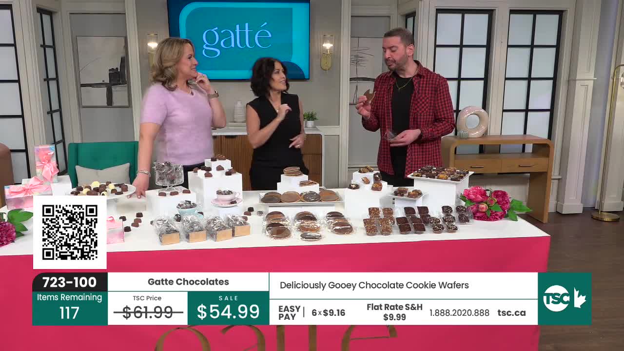 A man holds up a chocolate cookie wafer, gesturing to the display of Gatte Chocolates. Two women stand nearby, smiling as they discuss the treats.